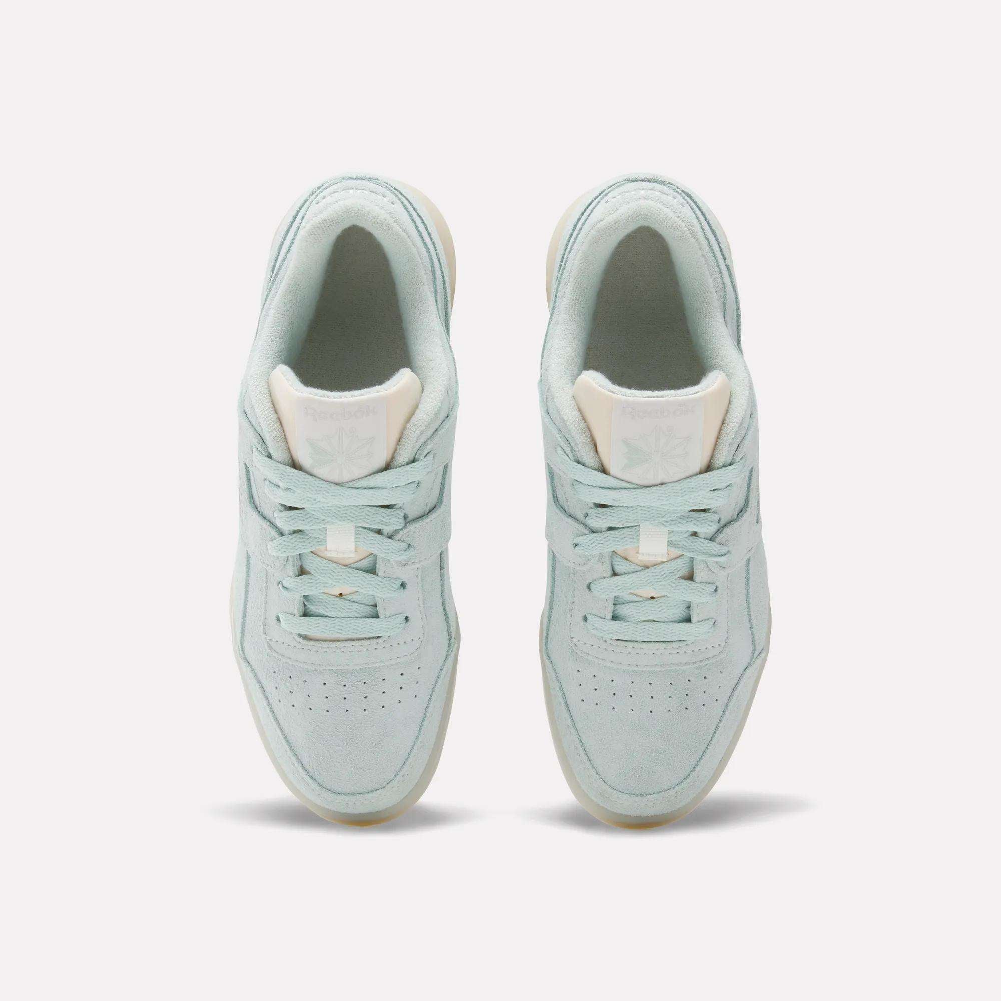 A pair of Reebok Women's Workout Plus Shoes in light blue with white soles and beige tongue labels, echoing 80s fitness style, are shown from above against a plain white background.