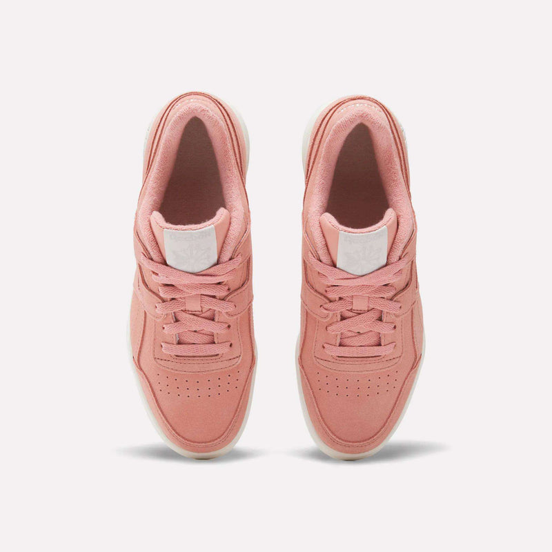 A pair of Women's Workout Plus Shoes by Reebok in pink with white soles, top view highlighting laces, perforated toes, and a white logo patch on the tongue—ideal for capturing vintage 80s workout style.
