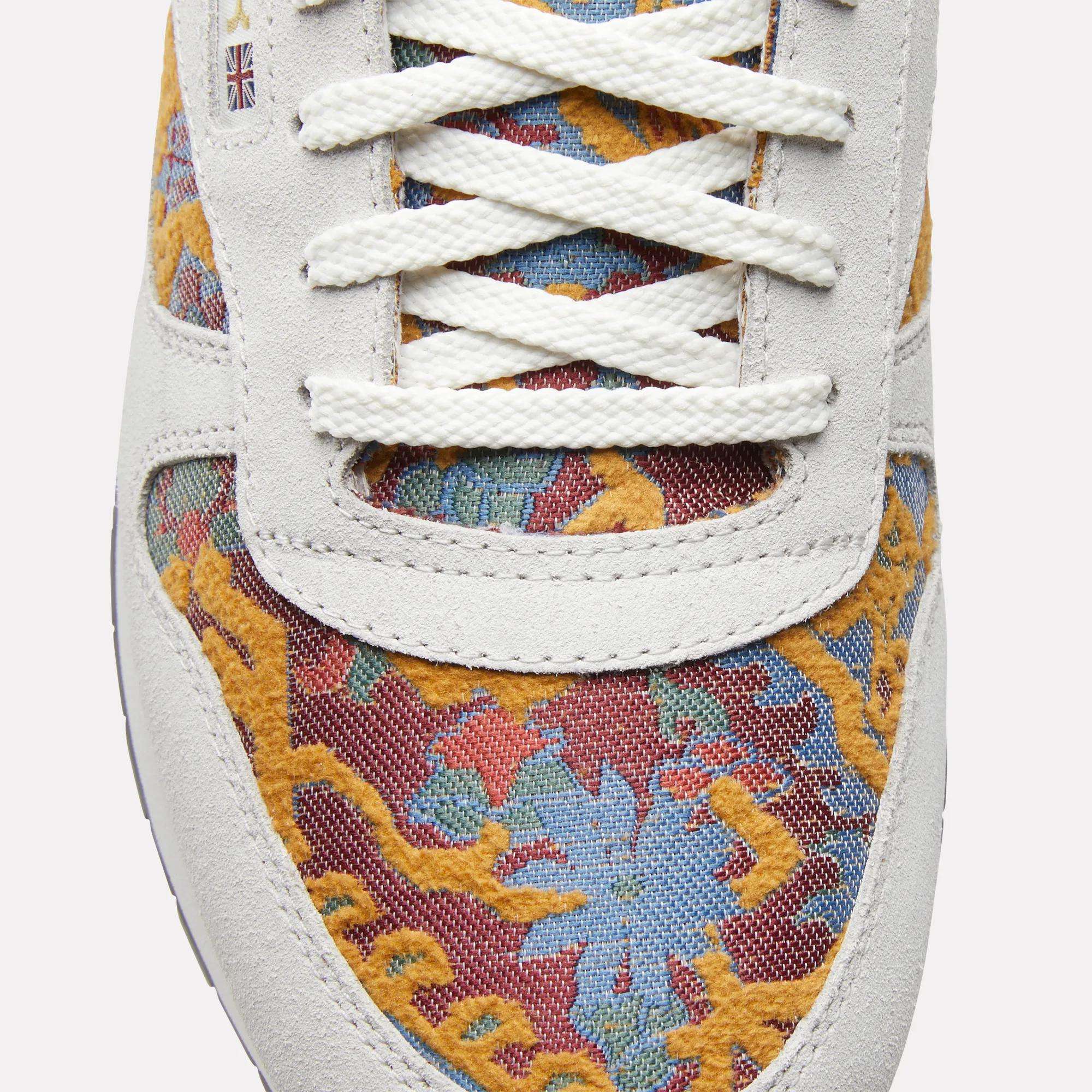 Close-up of Reebok Classic Leather 1983 Vintage Shoes with white laces, light suede trim, and a colorful yellow, blue, and red floral pattern. A small British flag patch near the laces adds to the retro look.