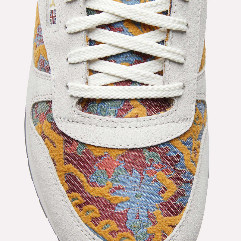 Close-up of Reebok Classic Leather 1983 Vintage Shoes with white laces, light suede trim, and a colorful yellow, blue, and red floral pattern. A small British flag patch near the laces adds to the retro look.