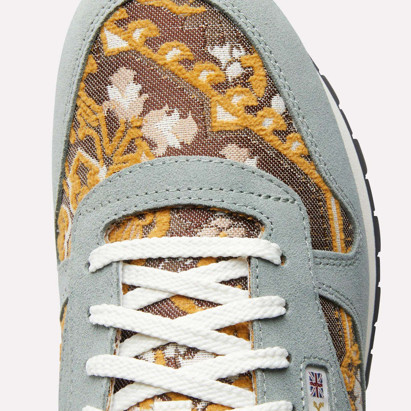 Close-up of the Reebok Classic Leather 1983 Vintage Shoes with yellow and white floral tapestry fabric, light gray suede overlays, white laces, and a Union Jack flag patch near the bottom lace eyelet—a retro-inspired detail.