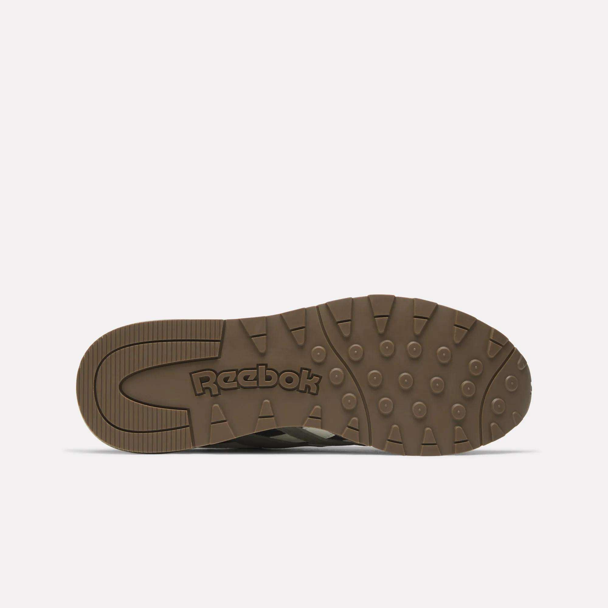 The image shows the bottom view of a brown Classic Nylon 89 Shoes sole by Reebok, featuring circular and rectangular grip patterns with the Reebok logo embossed in the center.