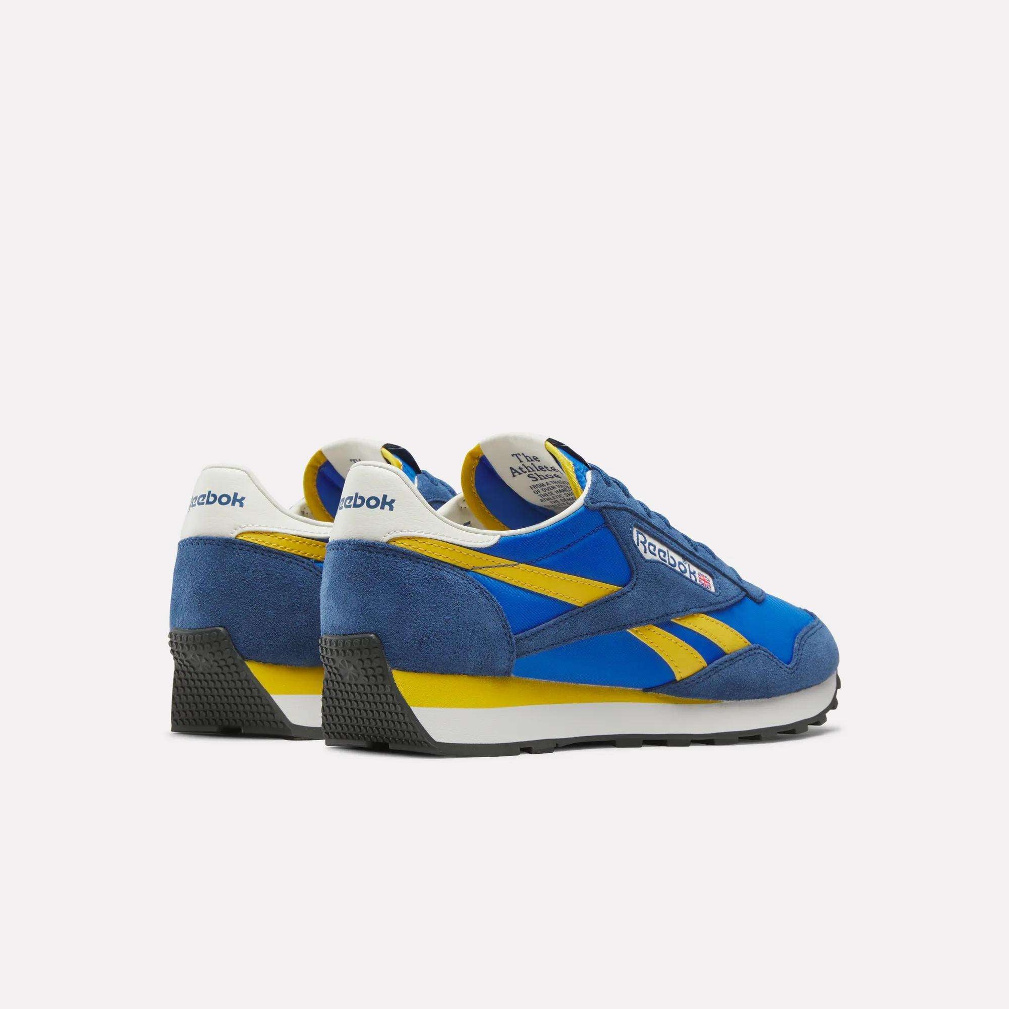 Reebok Aztec II Shoes in blue with yellow accents and white midsoles, featuring vintage running style, are shown angled from the back and side on a plain white background.