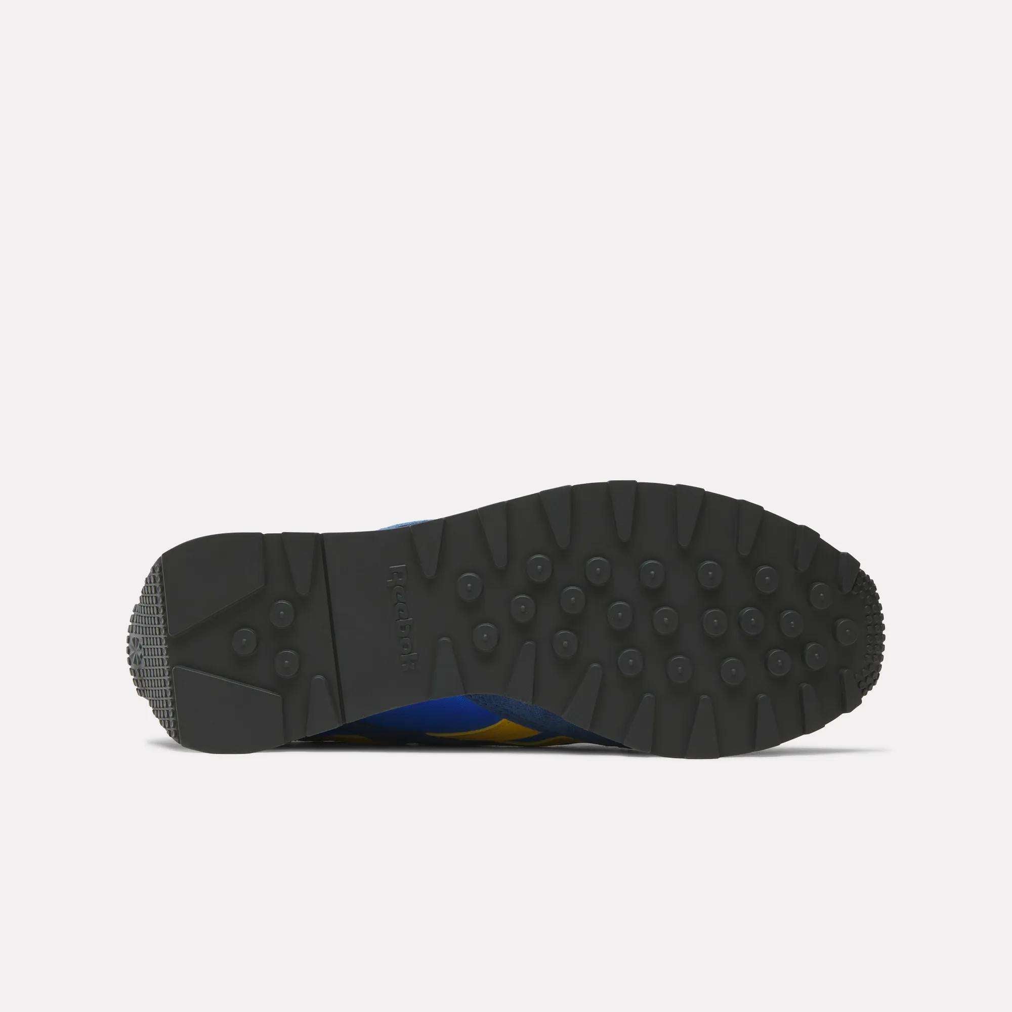 The image displays the black rubber sole of the Reebok Aztec II Shoes, featuring small round studs and a waffle heel pattern, highlighting vintage running style from the bottom view against a white background.