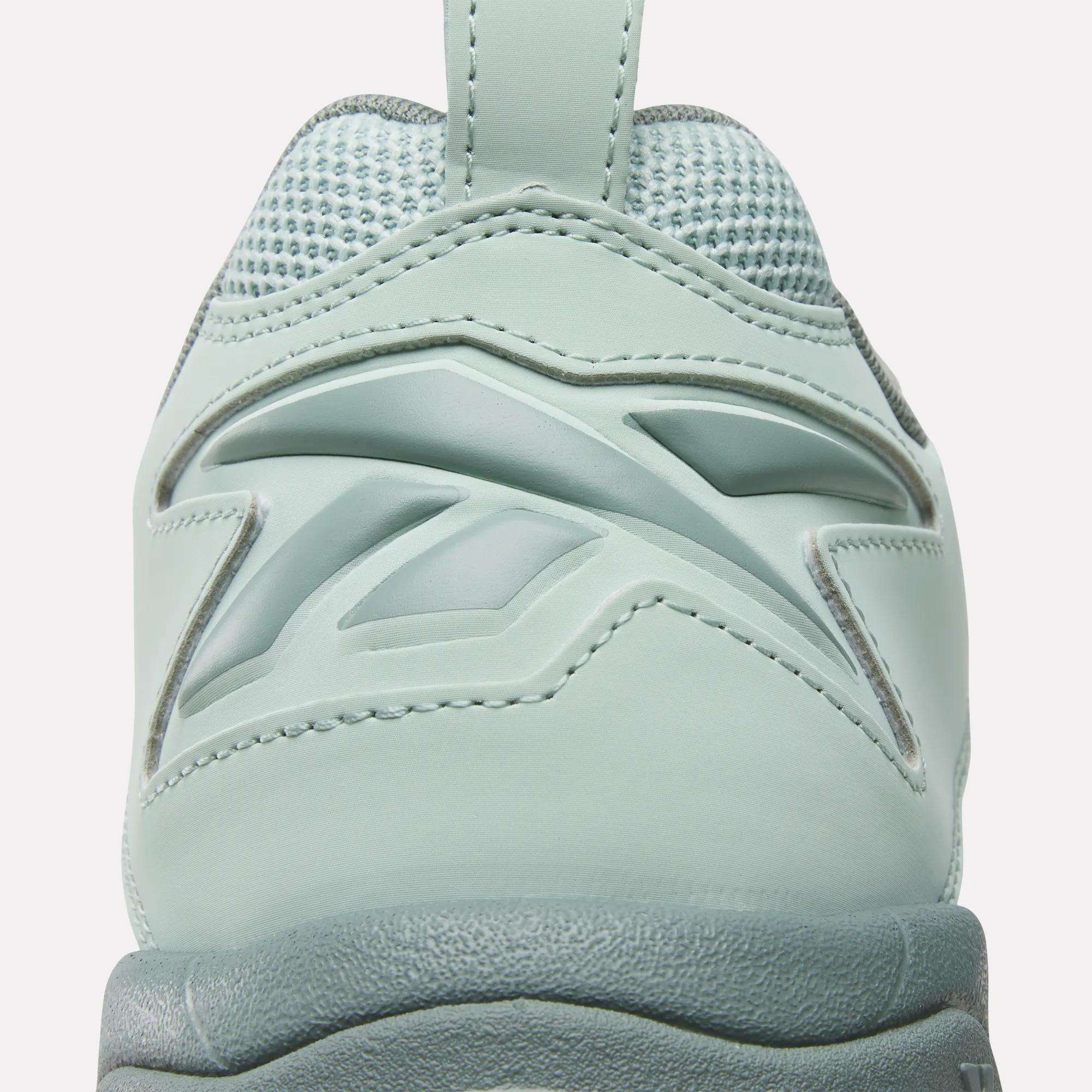 Close-up of the back of a light green Brutus Low Shoe by Reebok, featuring textured fabric, smooth synthetic overlays, and a stylish heel design—ideal for adding street style to your look.