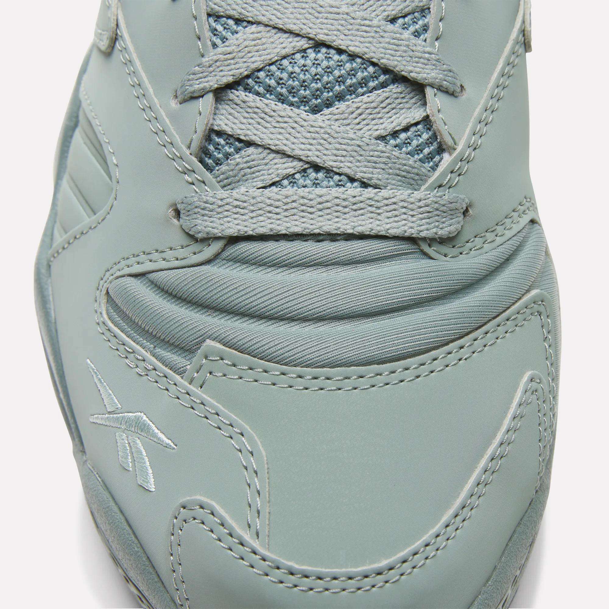 Close-up view of the toe and laces of the Brutus Low Shoes by Reebok, showcasing detailed stitching, logo embroidery, a mesh tongue, smooth synthetic overlays, and an EVA midsole for lightweight comfort.