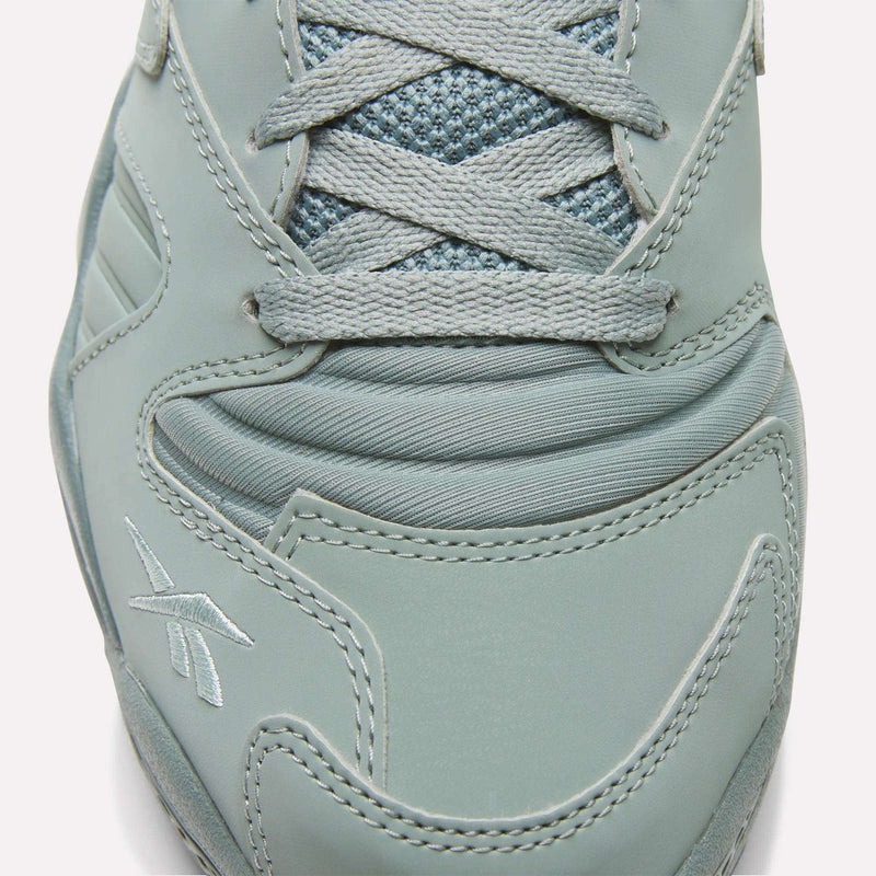 Close-up view of the toe and laces of the Brutus Low Shoes by Reebok, showcasing detailed stitching, logo embroidery, a mesh tongue, smooth synthetic overlays, and an EVA midsole for lightweight comfort.