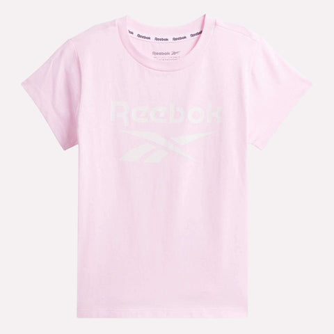 The Kids' ID Big Logo Tee by Reebok is a light pink, short-sleeve cotton jersey t-shirt for girls, featuring a faint white Reebok logo and text across the chest, shown flat on a plain background.