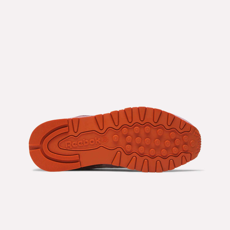 The image shows the orange rubber sole of the Reebok Women's Classic Leather Shoes from below, highlighting various tread patterns and the embossed Reebok logo near the heel.