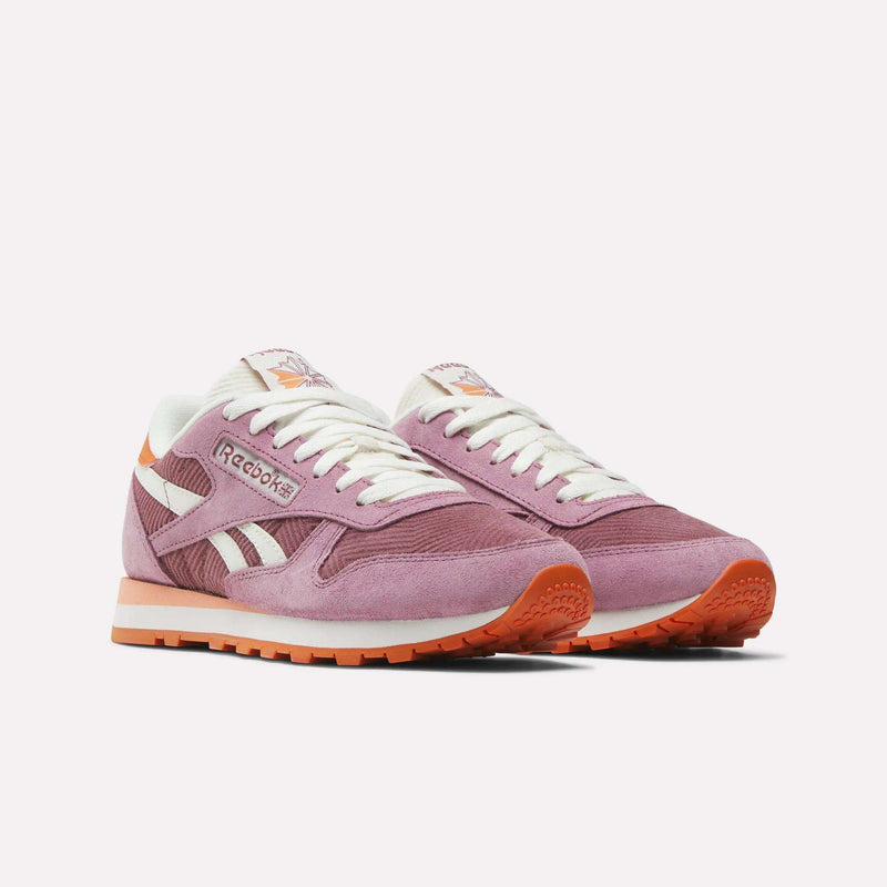 A pair of Reebok Women's Classic Leather Shoes in pink with white laces, orange accents, and orange outsoles is displayed against a plain white background.
