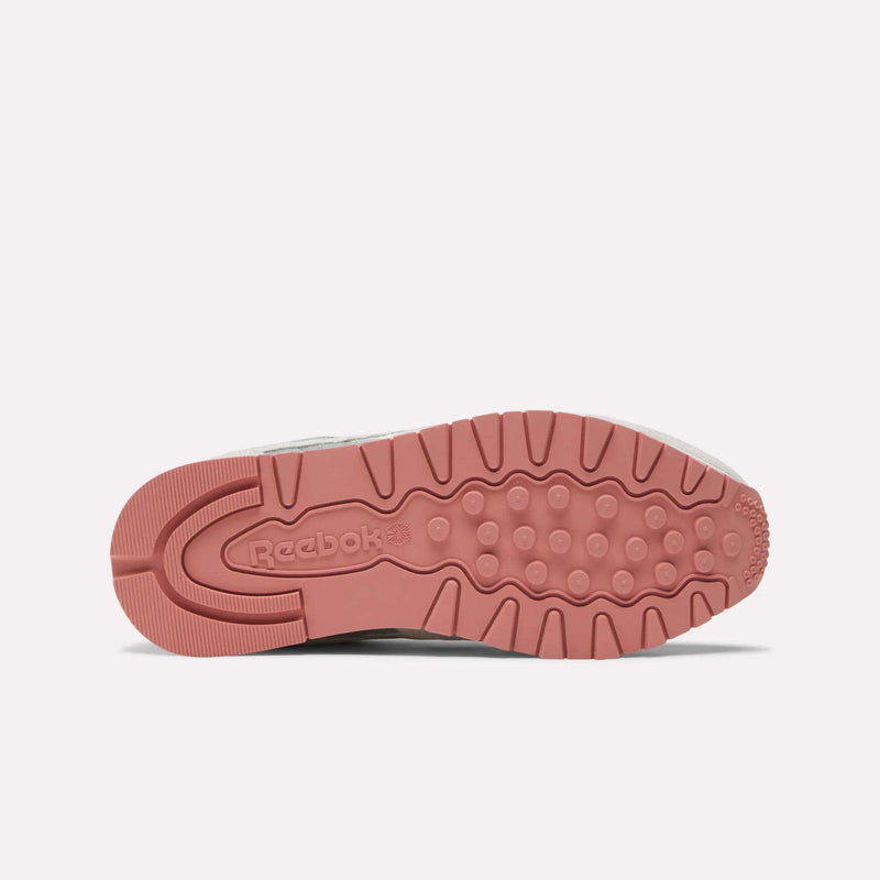 The image displays the underside of Reebok Women's Classic Leather Shoes, highlighting a pink rubber sole with circular and linear tread patterns and the Reebok logo embossed near the heel.