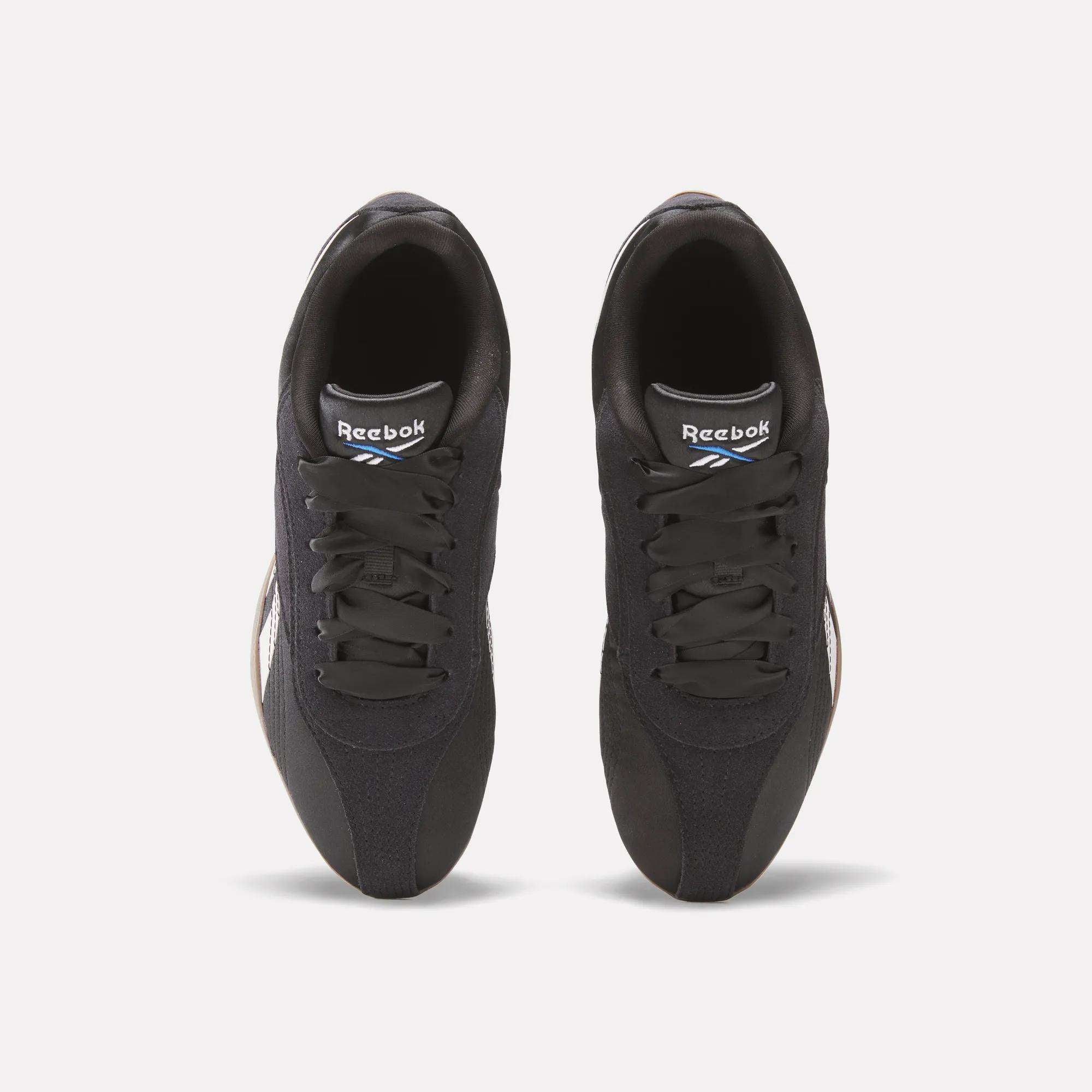 Top view of a pair of Women's Ultra Lo Shoes by Reebok in black, featuring black laces and white logos on the tongues, set against a light background for a sport-inspired style.