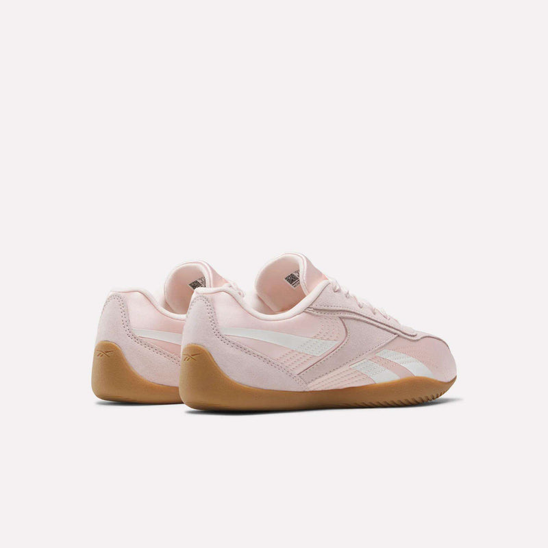 The Reebok Women's Ultra Lo Shoes feature a sport-inspired style in light pink with white stripes and gum soles, showcased at an angle with the heels forward against a plain white background.