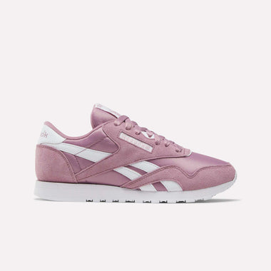 The Women's Classic Nylon Shoes by Reebok feature a pink retro design with white accents, logo, side stripes, and a white sole. Made from nylon and suede, they're shown in side profile against a plain light background.