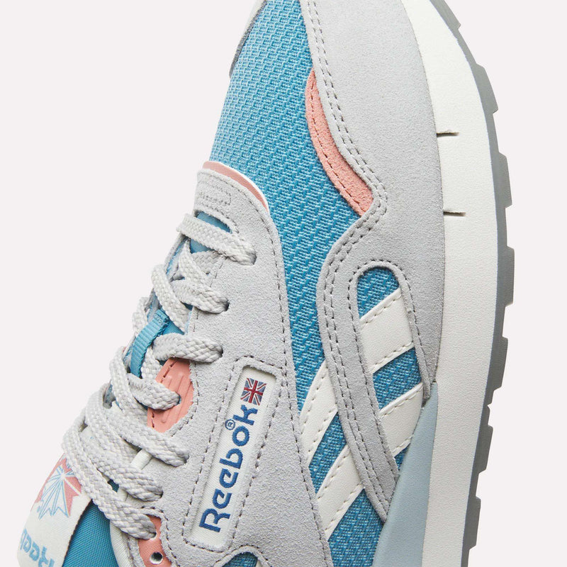 Close-up of the Reebok Women's Classic Nylon 89 Shoes, showcasing light grey suede overlays, blue mesh, white side stripes, a pink accent near the laces, and the iconic Reebok logo with a UK flag on the side.
