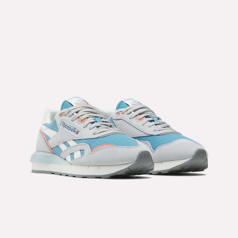 The Reebok Women's Classic Nylon 89 Shoes are running sneakers in light gray, blue, and white with pink accents. They feature a retro style, lace-up closure, and Reebok branding on the side and tongue against a white background.