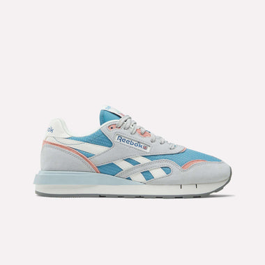The Reebok Women's Classic Nylon 89 Shoes feature a retro look with light blue mesh, grey suede overlays, white and pink accents, plus the Reebok logo on the side and tongue. Shown on a white background—ideal for classic running shoe fans.