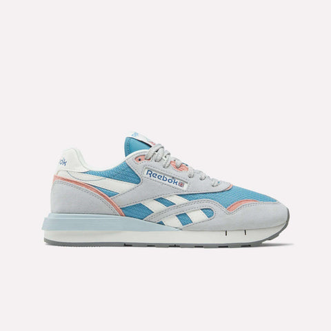 The Reebok Women's Classic Nylon 89 Shoes feature a retro look with light blue mesh, grey suede overlays, white and pink accents, plus the Reebok logo on the side and tongue. Shown on a white background—ideal for classic running shoe fans.