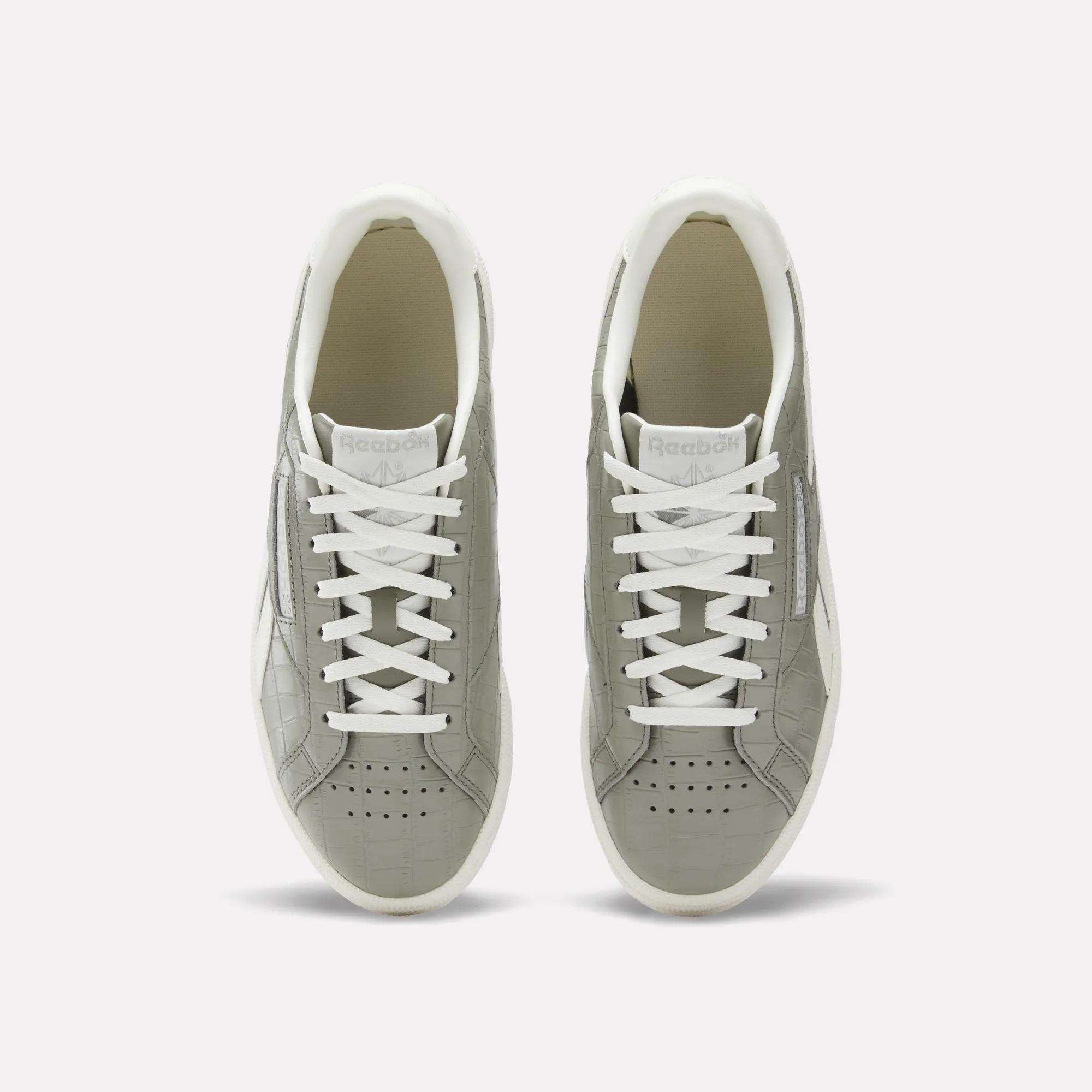 A pair of Reebok Women's Club C Grounds UK shoes in grey with white laces and soles, shown from above on a plain white background. These court-inspired shoes have perforated toes and a clean white inner lining.