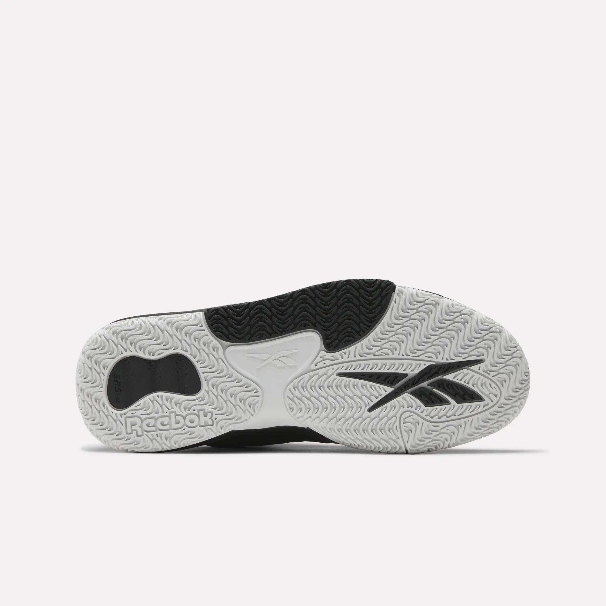 The image shows the sole of Reebok Engine LT Shoes, featuring a textured white, black, and grey rubber outsole with various tread patterns and the Reebok logo clearly visible.