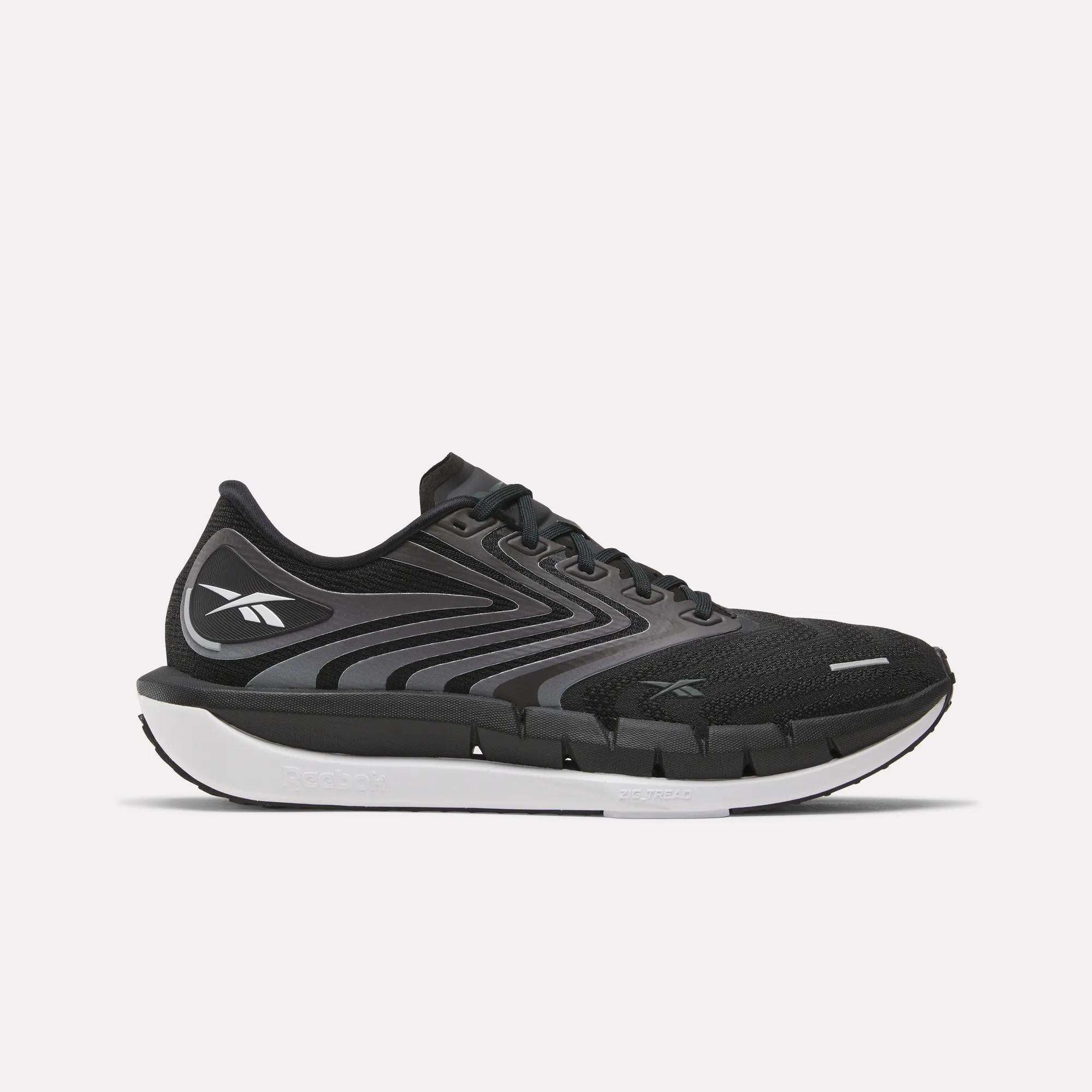 The Reebok Men's FloatZig Tread Running Shoes feature a black and gray design with a white sole, black laces, and a cushioned midsole, ideal for treadmill workouts. The Reebok logo is on the side against a plain white background.