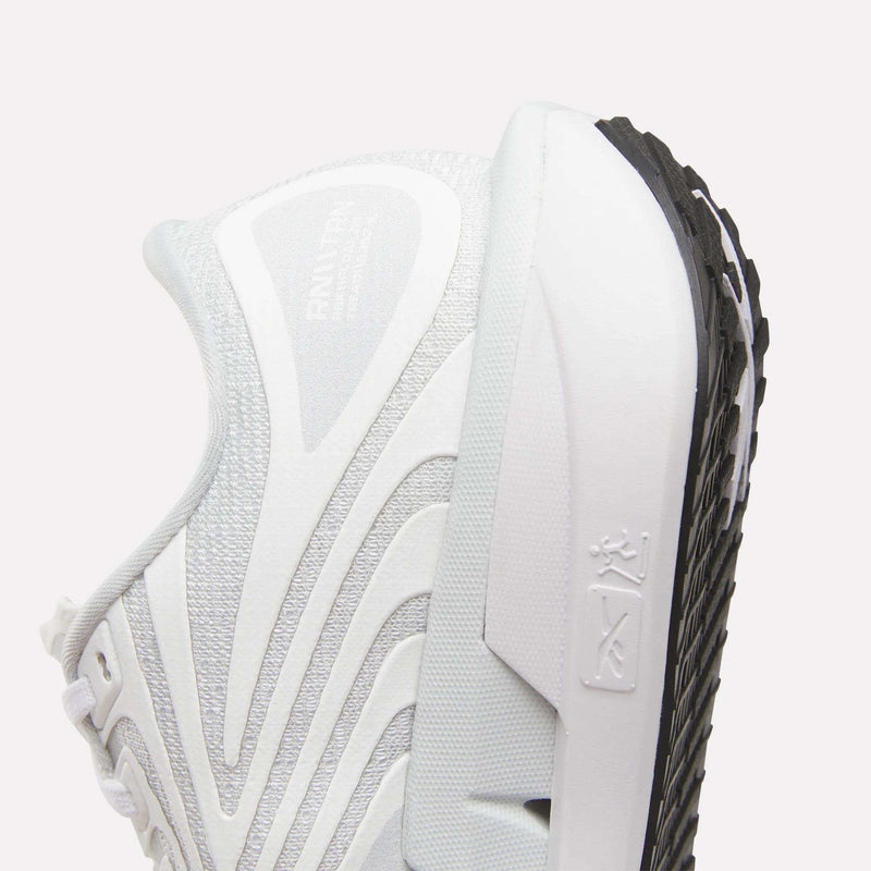 Close-up of Reebok Women's FloatZig Tread Running Shoes in white and gray with wavy silver accents. Features breathable mesh, textured details, visible sole, and embossed logo on the midsole against a pale background.