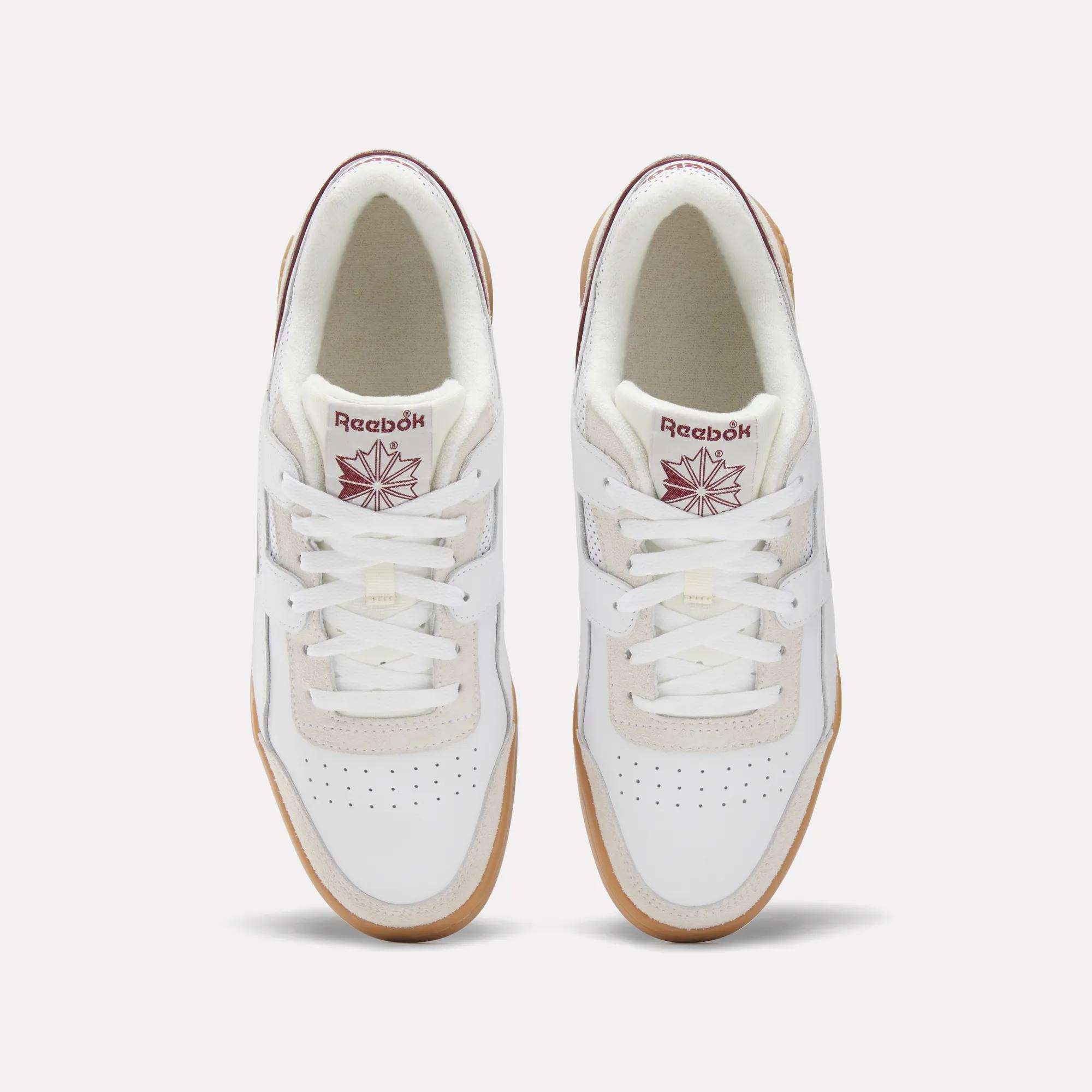 Top view of Reebok Workout Plus Shoes in white with gum soles, maroon Reebok logos on the tongues, and perforated toe boxes, evoking classic '80s fitness style against a light background.