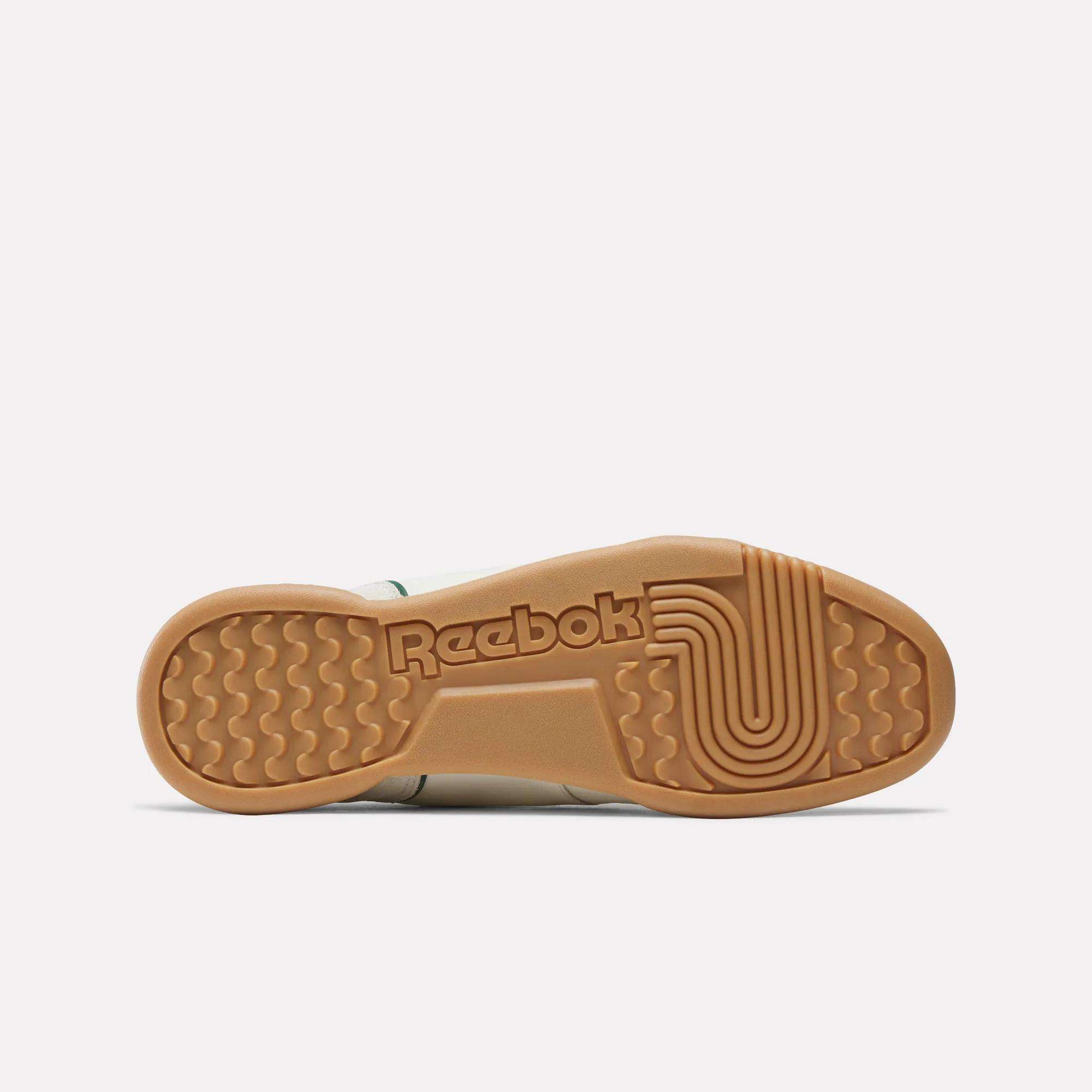 The sole of the Reebok Workout Plus Shoes is pictured, displaying a tan rubber bottom with the Reebok logo and grooved traction patterns, highlighting classic '80s fitness style on a plain white background.