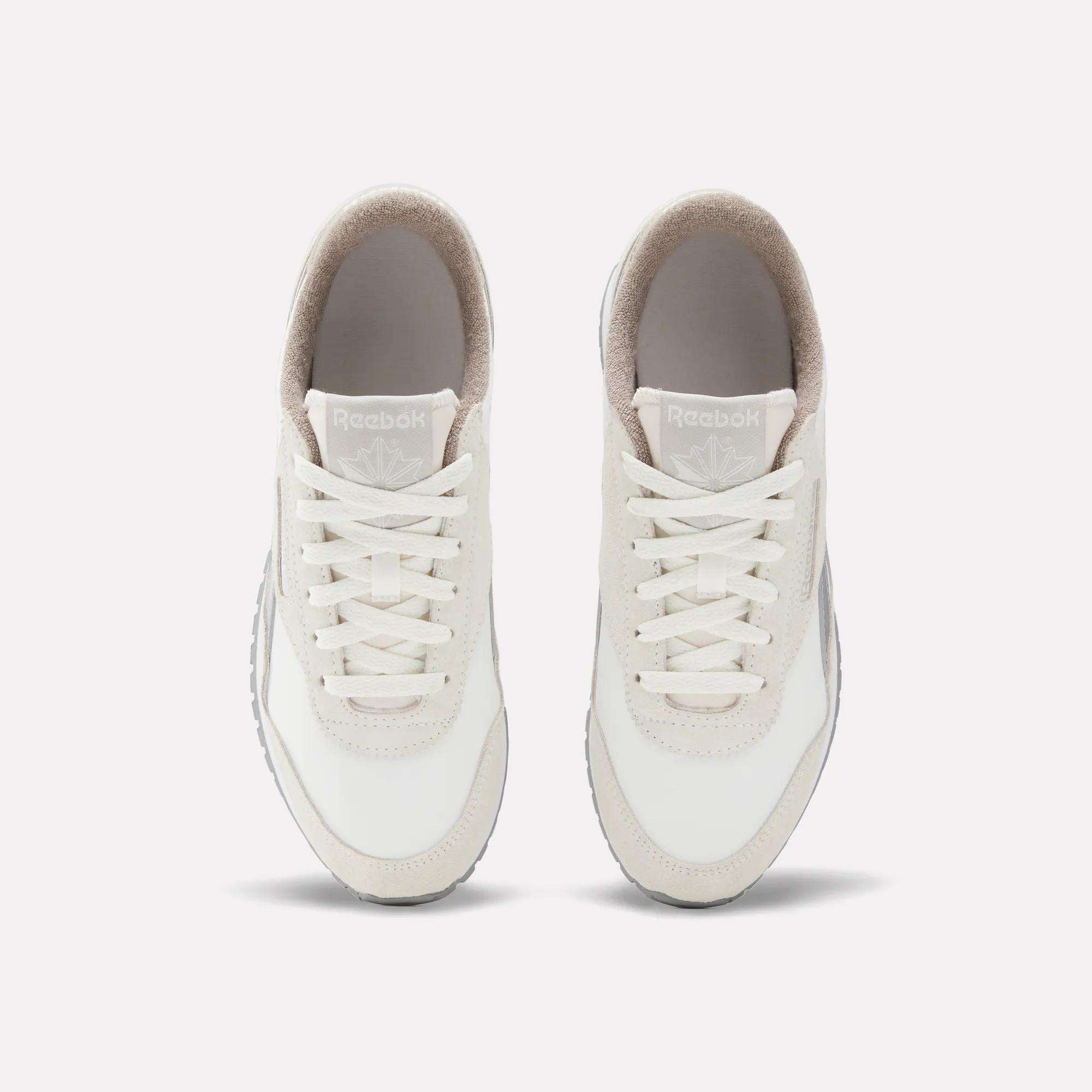 The Reebok Women's Classic AZ Shoes, in white with beige accents, are shown from above with visible laces, tongue, and Reebok branding. These vintage-style sneakers are placed side by side on a plain light background.