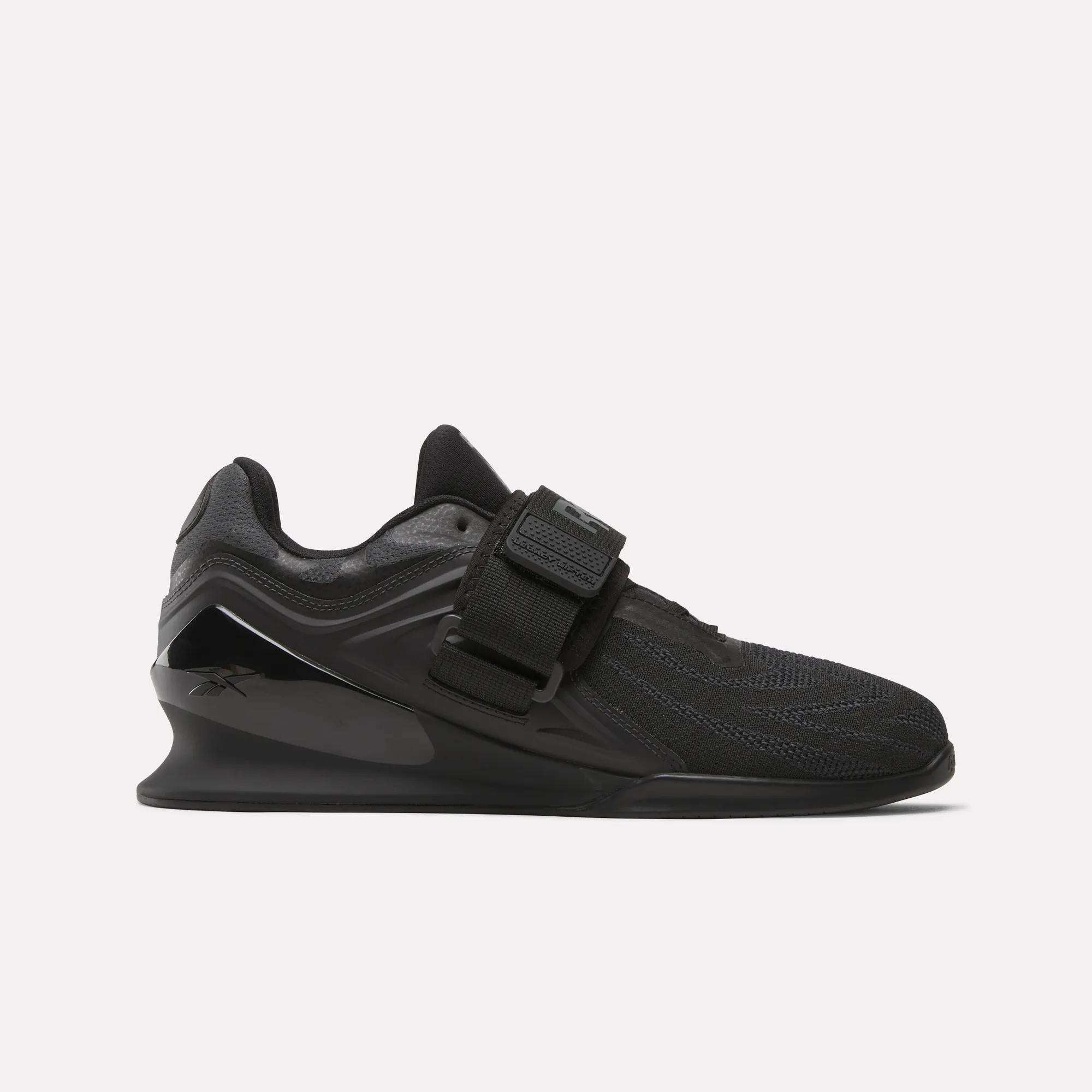 The Reebok Men's Legacy Lifter IV Shoes feature a black textured mesh upper, thick sole, and wide midfoot strap for added stability, displayed in side profile against a plain white background.