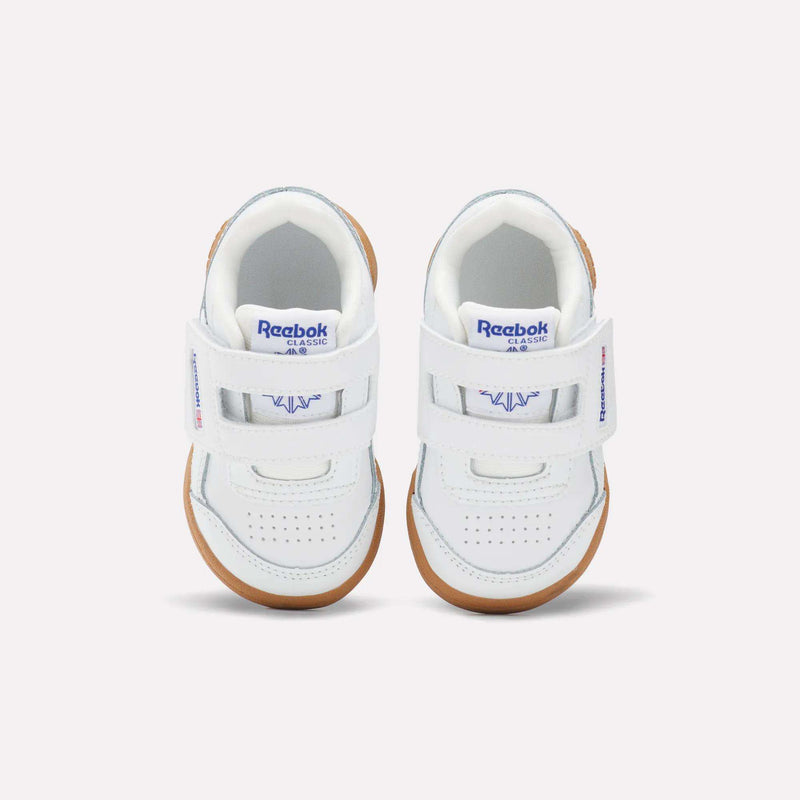 The Reebok Kids' Workout Plus Shoes for babies and toddlers feature an H-strap design, white upper, blue Reebok branding, and light brown rubber soles, shown from above on a plain light background.
