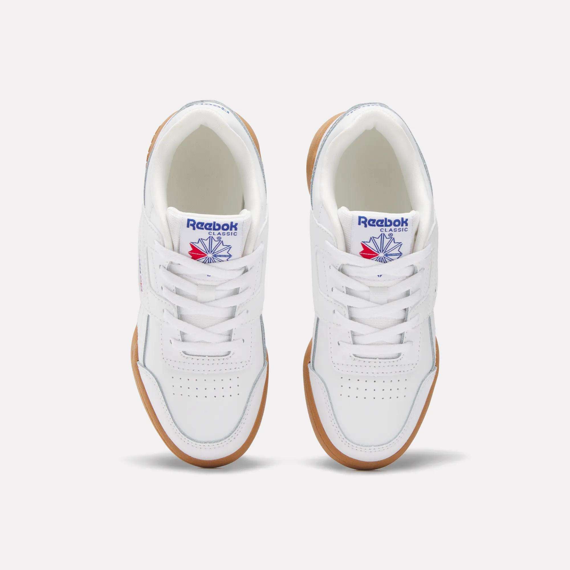 A pair of white Reebok Workout Plus Shoes for little kids, seen from above. They have gum soles, white laces, toe perforations, and display the blue and red Reebok logo on the tongue.