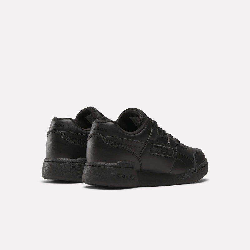 A pair of Reebok Workout Plus Shoes for little kids, shown in black from the back and side. These low-top sneakers feature laces and Reebok branding on the heel and side, displayed against a plain white background.