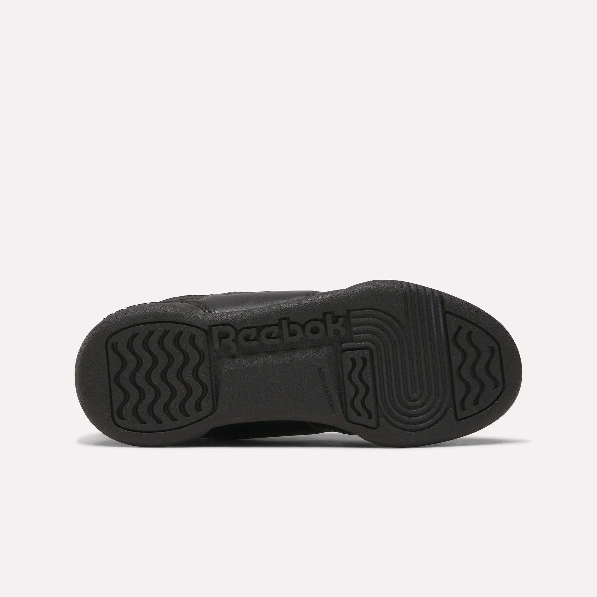The image shows the black rubber sole of Reebok Workout Plus Shoes for little kids, viewed from the bottom, with wavy and straight tread patterns and the Reebok logo embossed in the center.