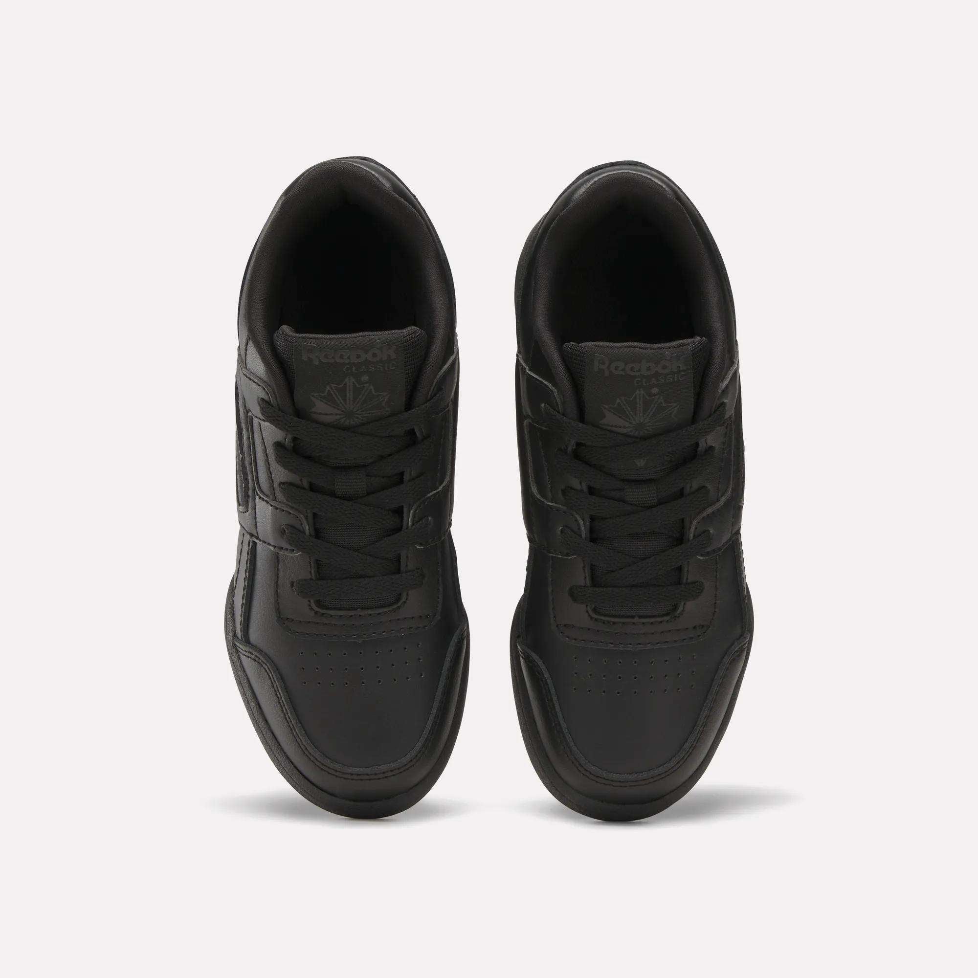 A pair of Reebok Workout Plus Shoes for little kids in black, shown from above on a white background, highlighting the laces, stitched details, and Reebok logos on the tongues.