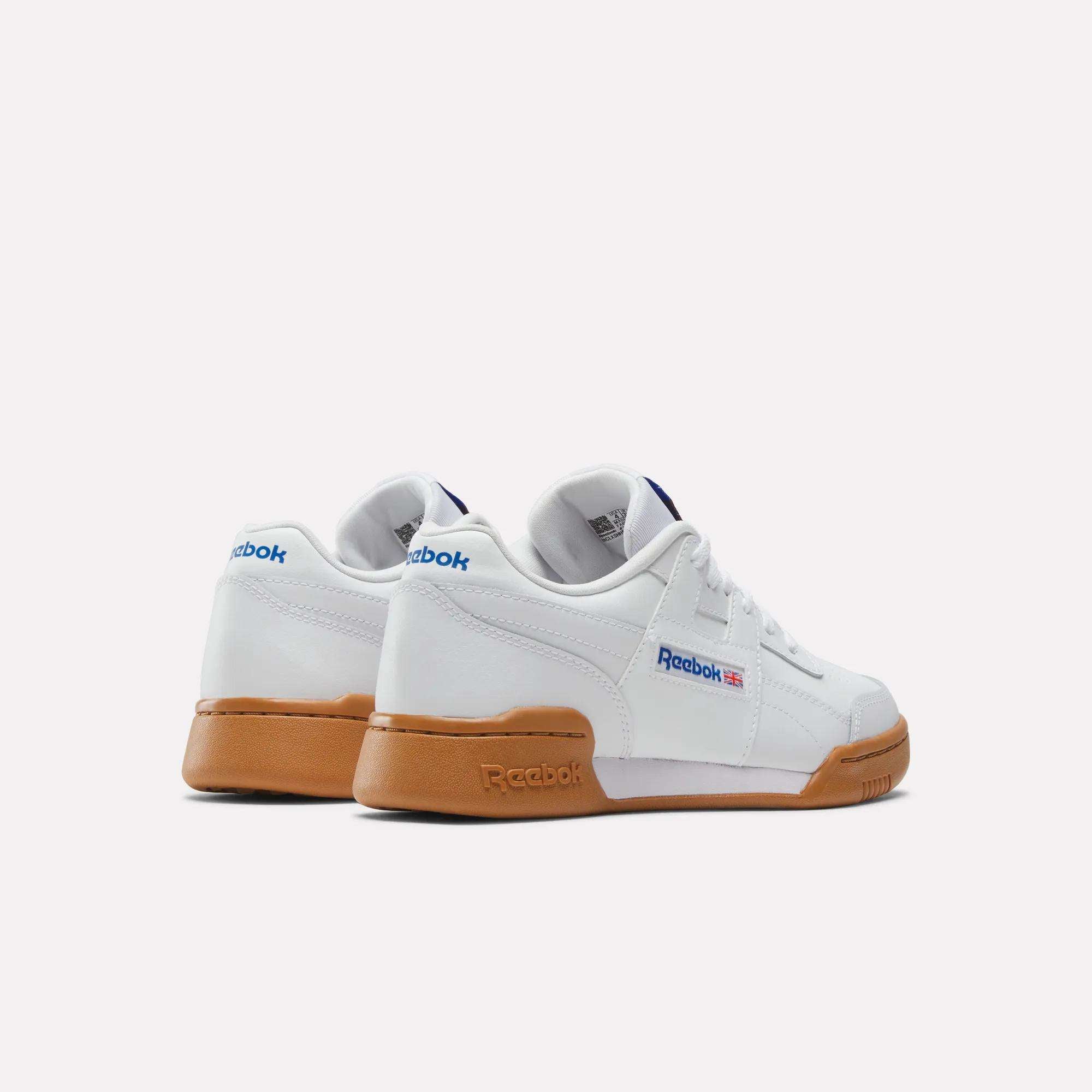 A pair of Reebok Workout Plus Shoes for big kids, in white with brown gum soles, blue Reebok logos, and small British flags on the sides, displayed against a plain white background.