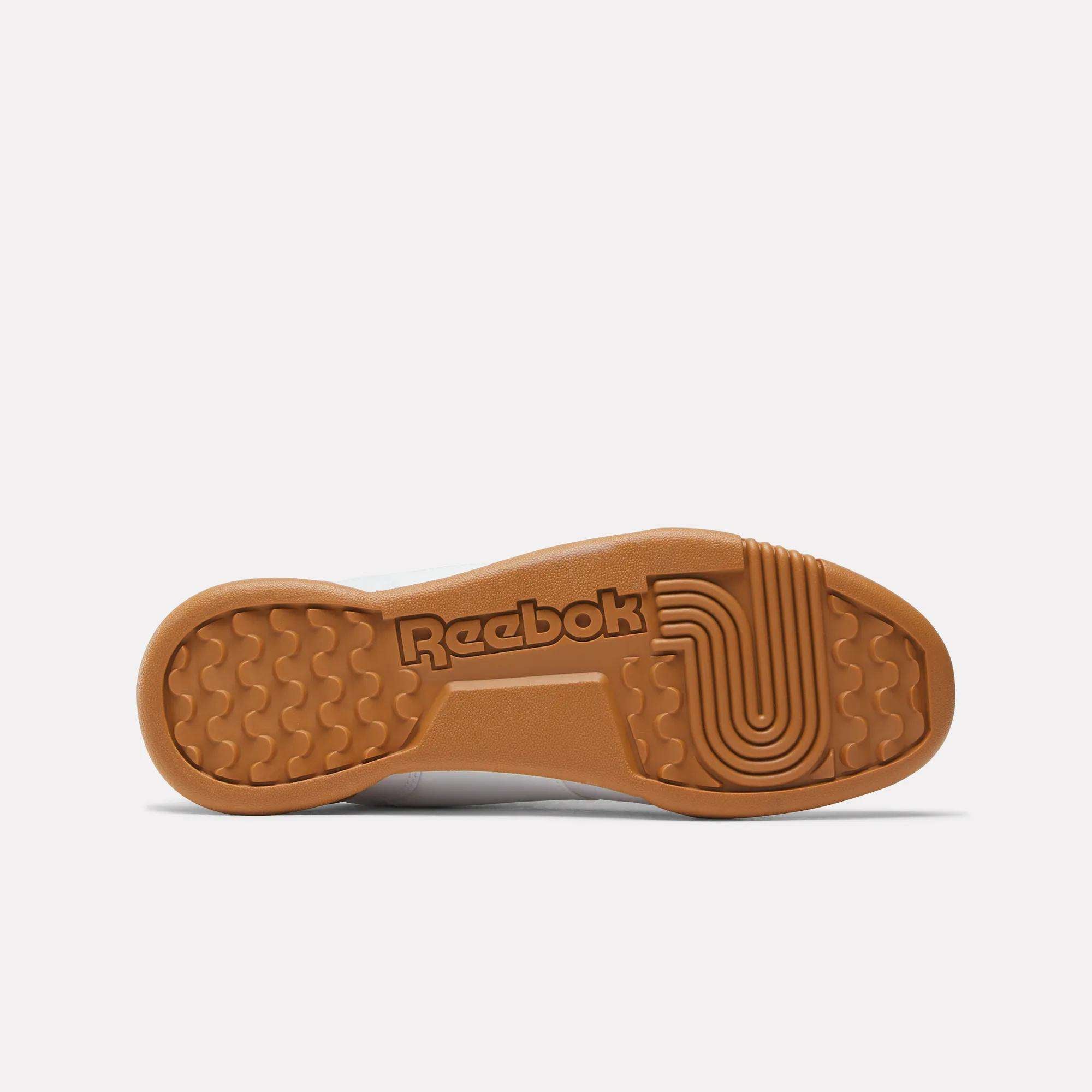 The image shows the gum-colored rubber sole of the Reebok Workout Plus Shoes for Big Kids, featuring a central Reebok logo and multiple textured grip patterns to enhance traction.