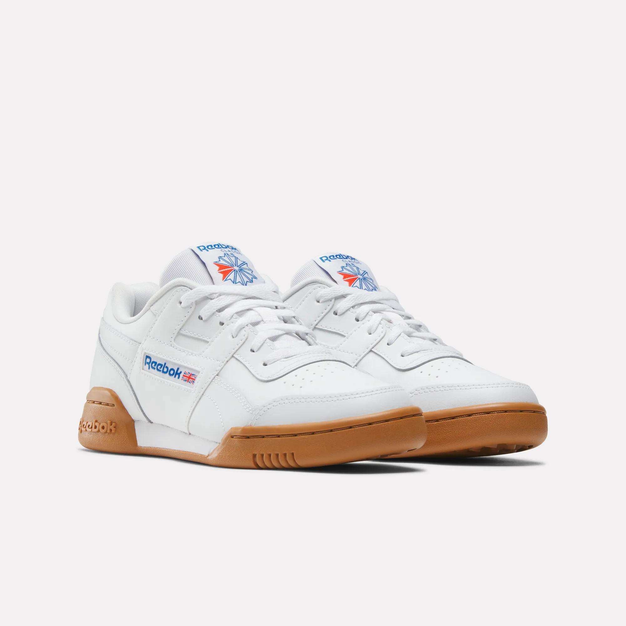 A pair of Reebok Workout Plus Shoes for big kids in white, with gum-colored soles and signature logos on the side and tongue, displayed against a plain white background.