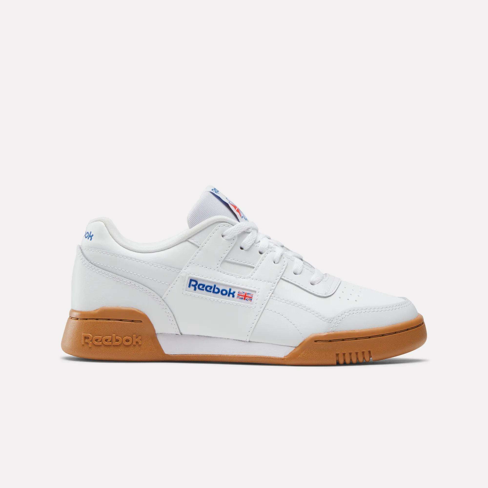 The Reebok Workout Plus Shoes - Big Kids is shown from the left in white with a gum sole, blue Reebok branding, and a small Union Jack flag—ideal sporty sneakers for kids who love classic style.