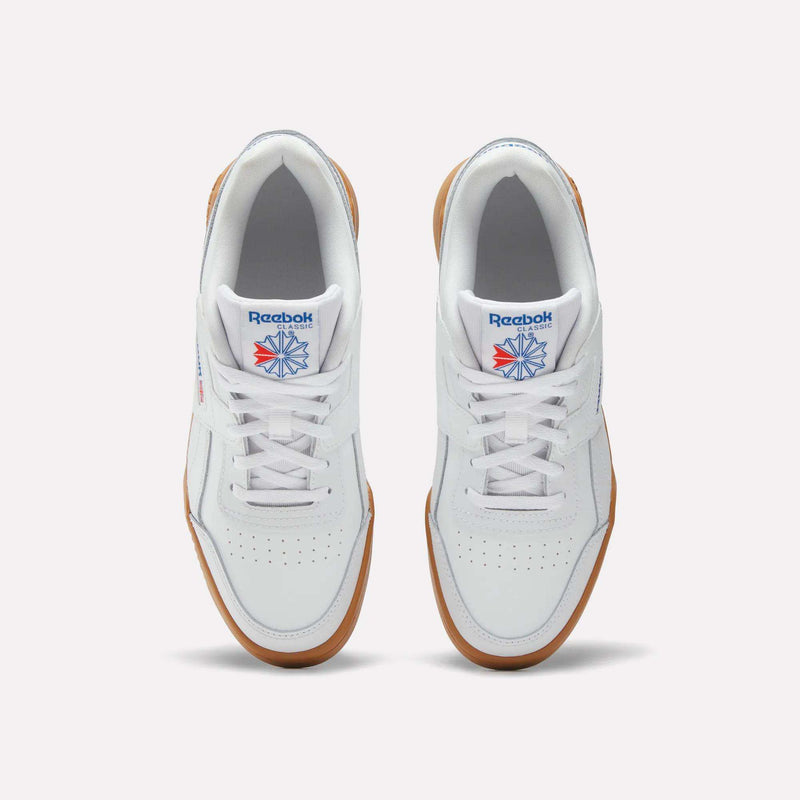 Top view of Reebok Workout Plus Shoes for big kids, featuring white retro uppers with gum soles, white laces, and blue and red Reebok logos on the tongues, placed side by side on a plain light background.