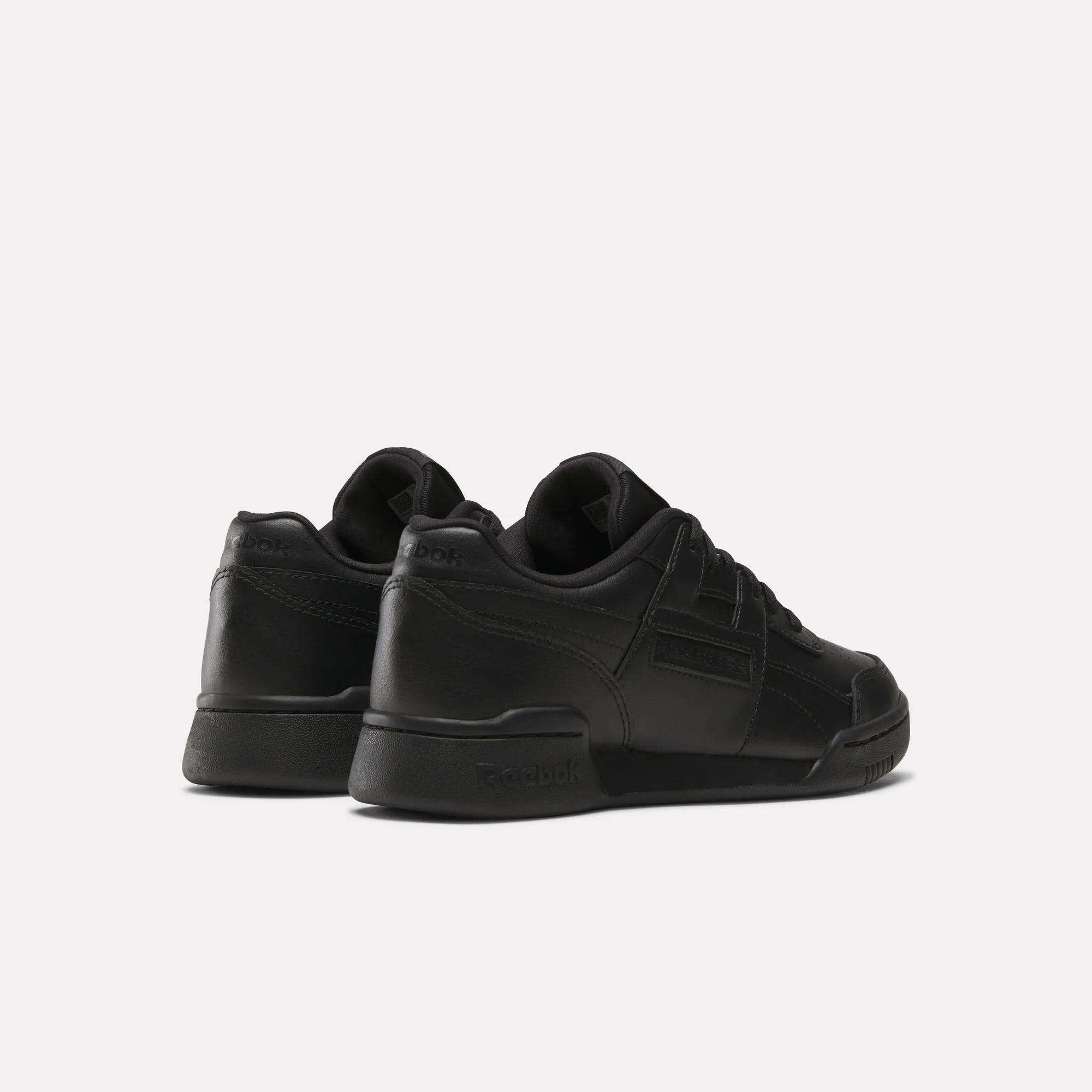 The Reebok Workout Plus Shoes for Big Kids, in black with a low-top design, are displayed from back and side angles on a plain light background, bringing retro energy to juniors' sporty footwear.