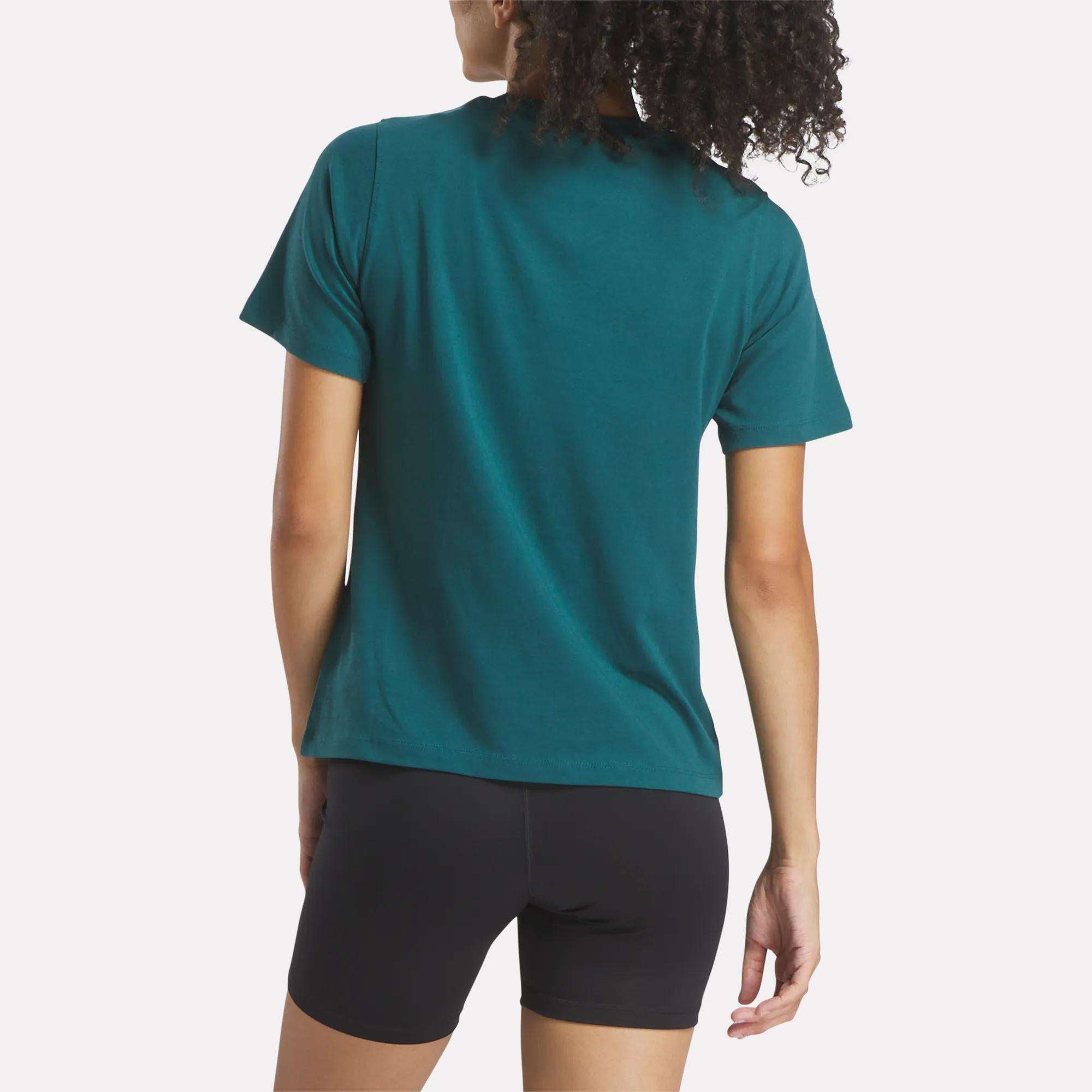 A person with curly hair is seen from the back, wearing a Reebok Women's Two-Color Logo Crew Short Sleeve Tee with black fitted shorts, standing against a plain white background.
