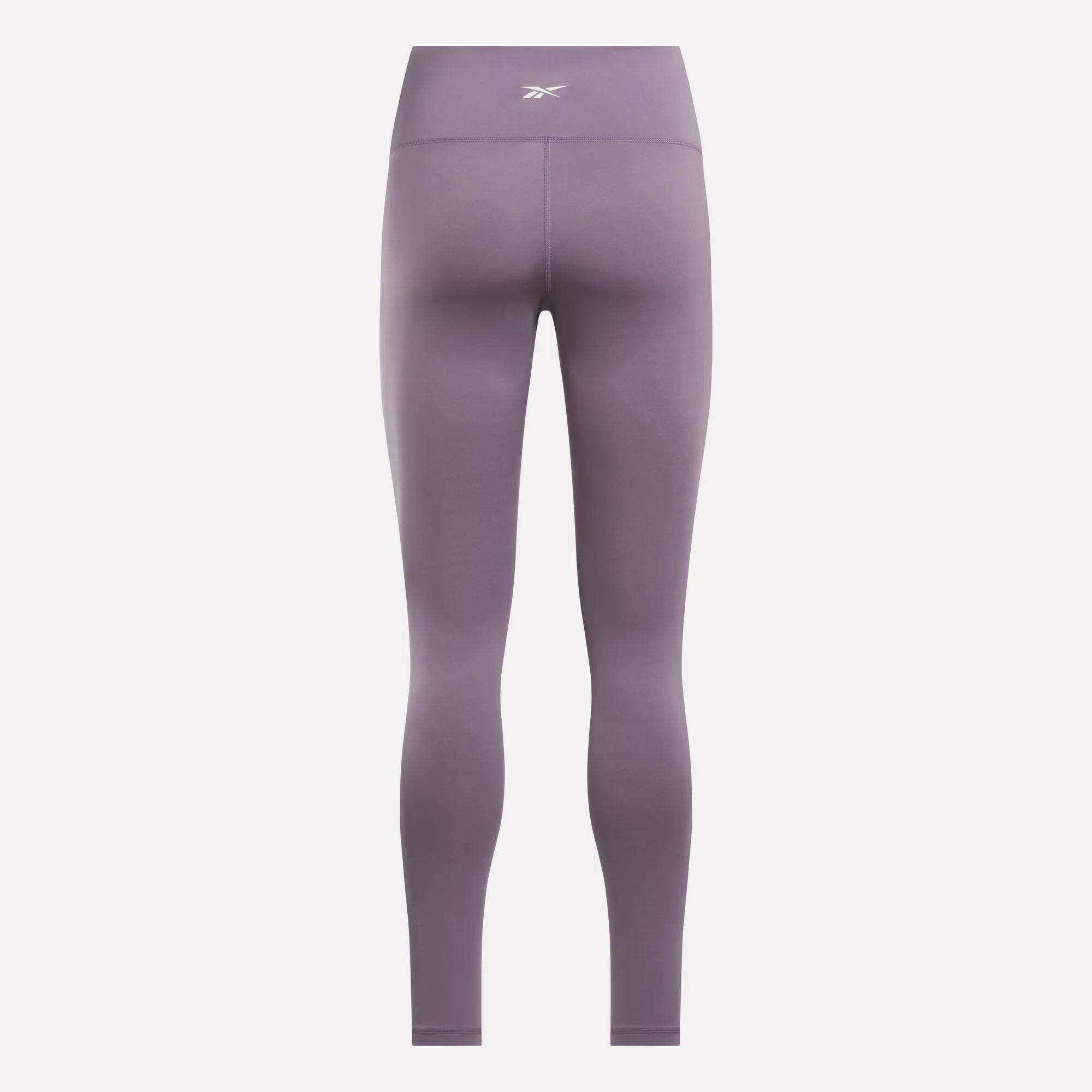 The Women's Core High-Rise Leggings by Reebok are shown from the back in purple, featuring a small white logo on the high waistband and made from moisture-wicking RBK-DRY fabric for comfort against a plain light background.