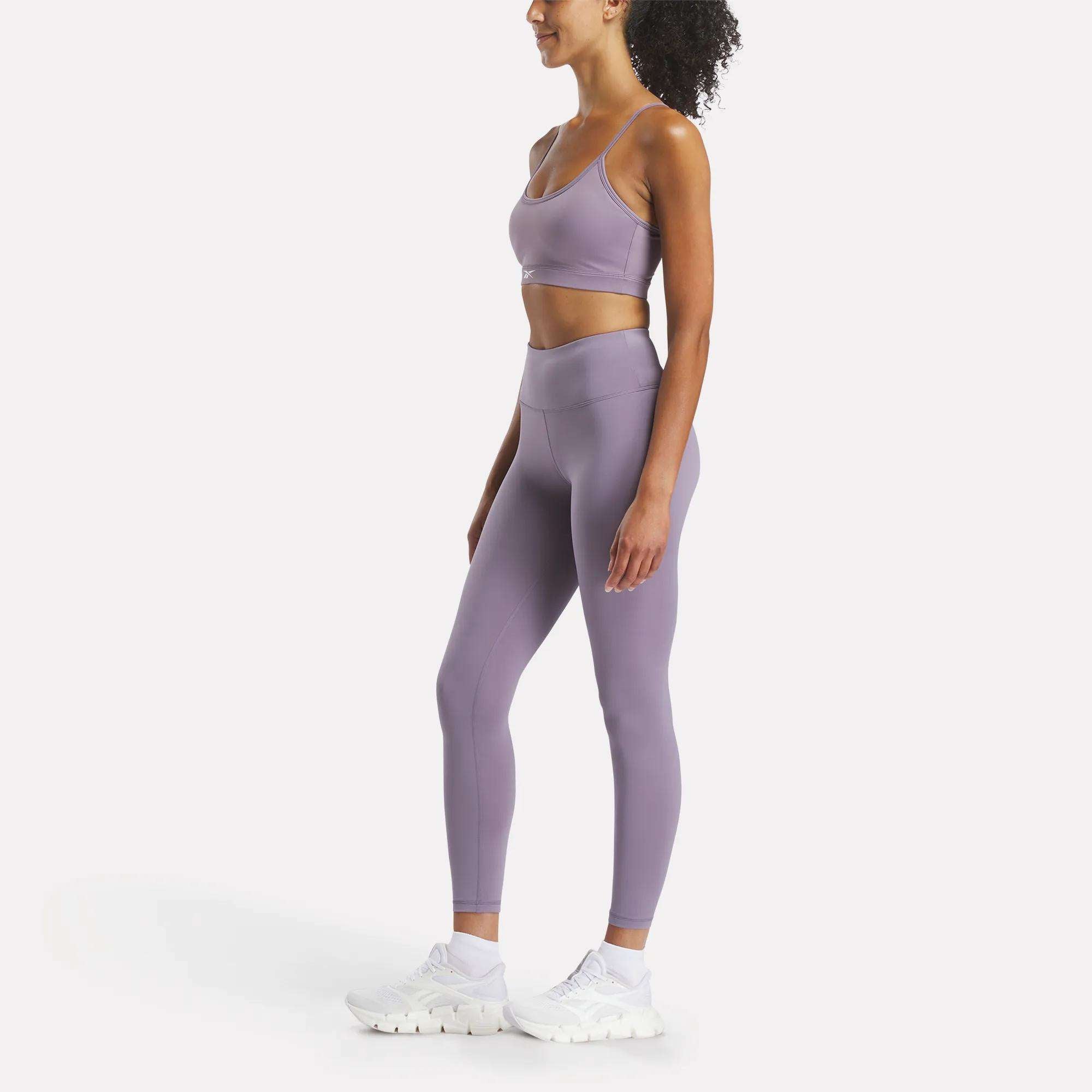 A woman in a purple outfit models Reebok’s Women’s Core High-Rise Leggings, designed for both style and performance.