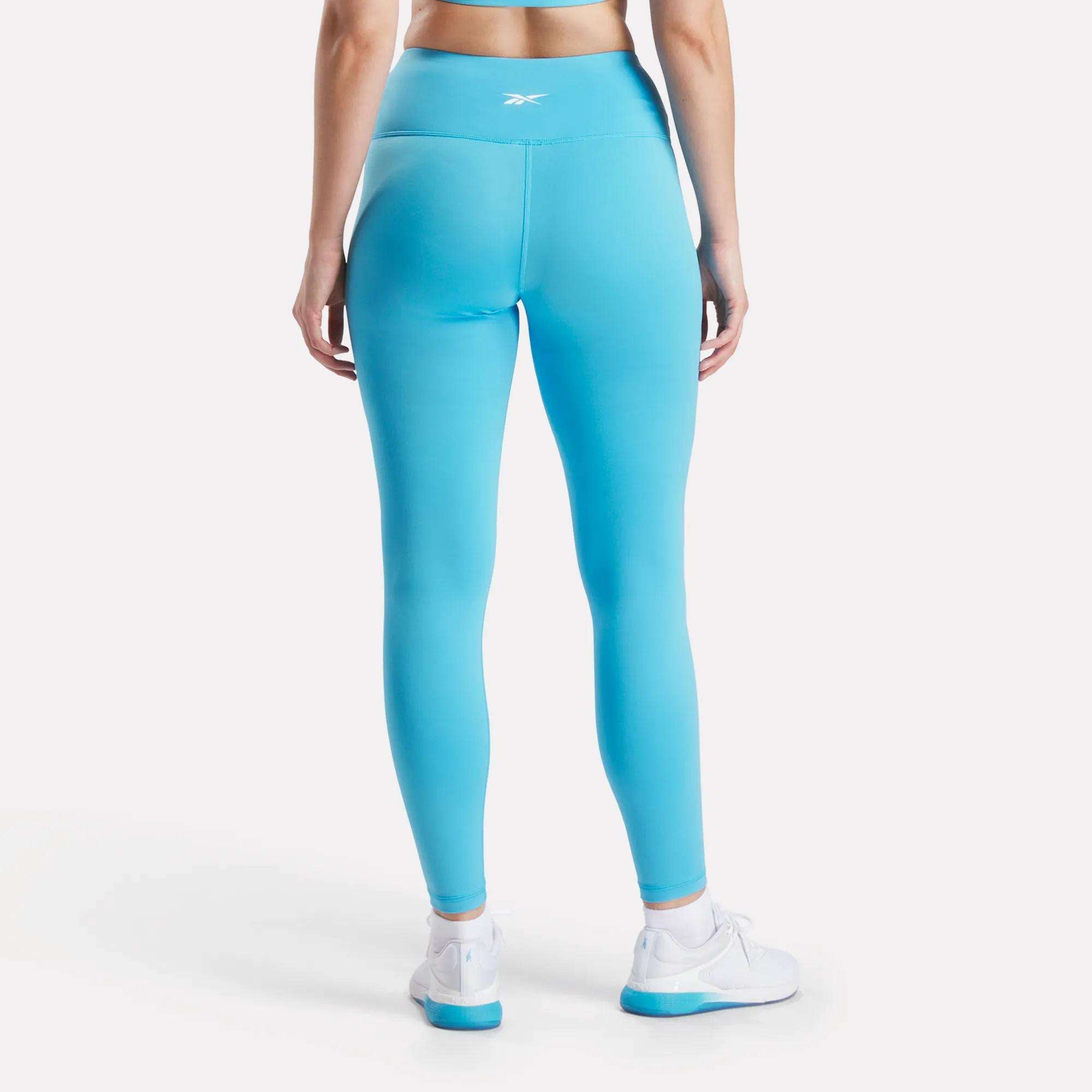 A woman wears Reebok Women's Core High-Rise Leggings in blue, featuring RBK-DRY fabric.