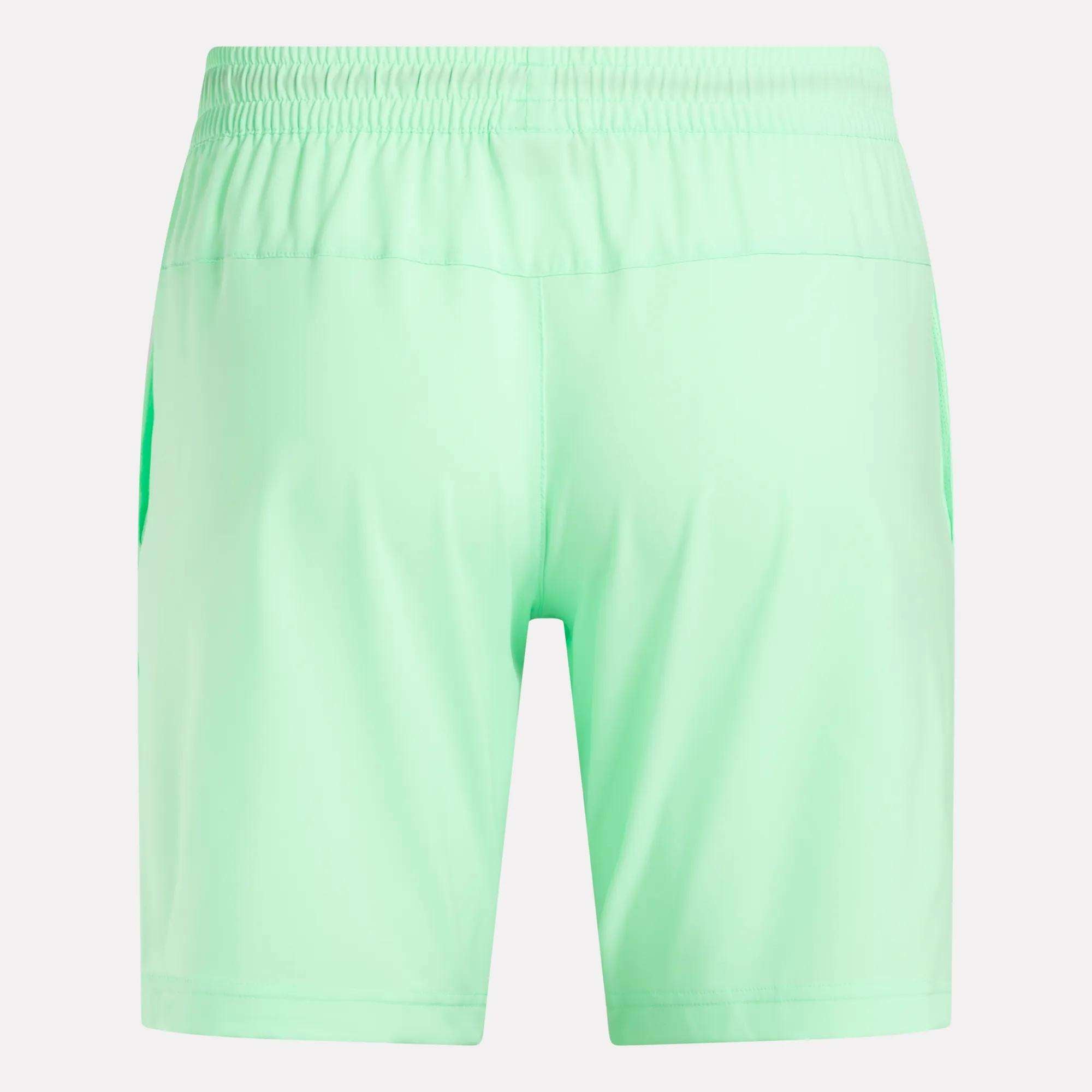Back view of Reebok Men's Workout Ready Woven Shorts in light green, featuring an elastic waistband and side pockets. These sweat-wicking workout shorts are displayed on a plain white background.