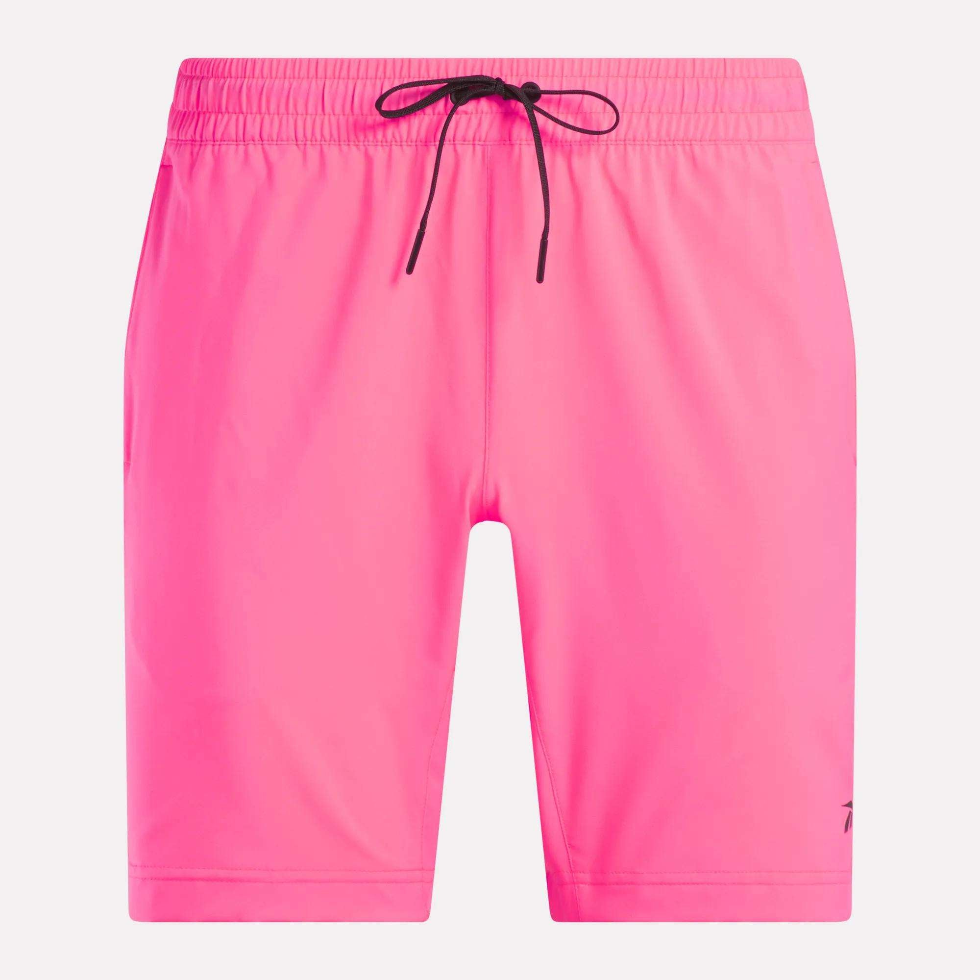 Men's Workout Ready Woven Shorts by Reebok in bright pink, featuring an elastic waistband, black drawstring, and subtle black logo on the lower left leg. Designed for sweat-wicking workouts. Displayed on a plain white background.