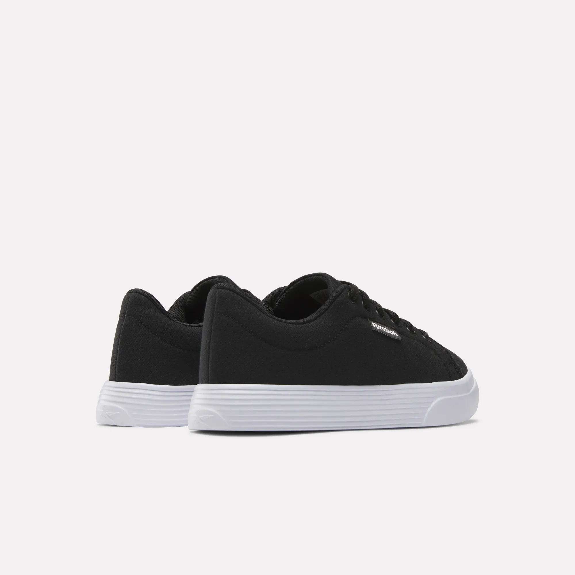 The Women's OnLux Court Lite Walking Shoes by Reebok are black low-top, comfortable walking shoes with white rubber soles, displayed from the back and side on a plain white background.