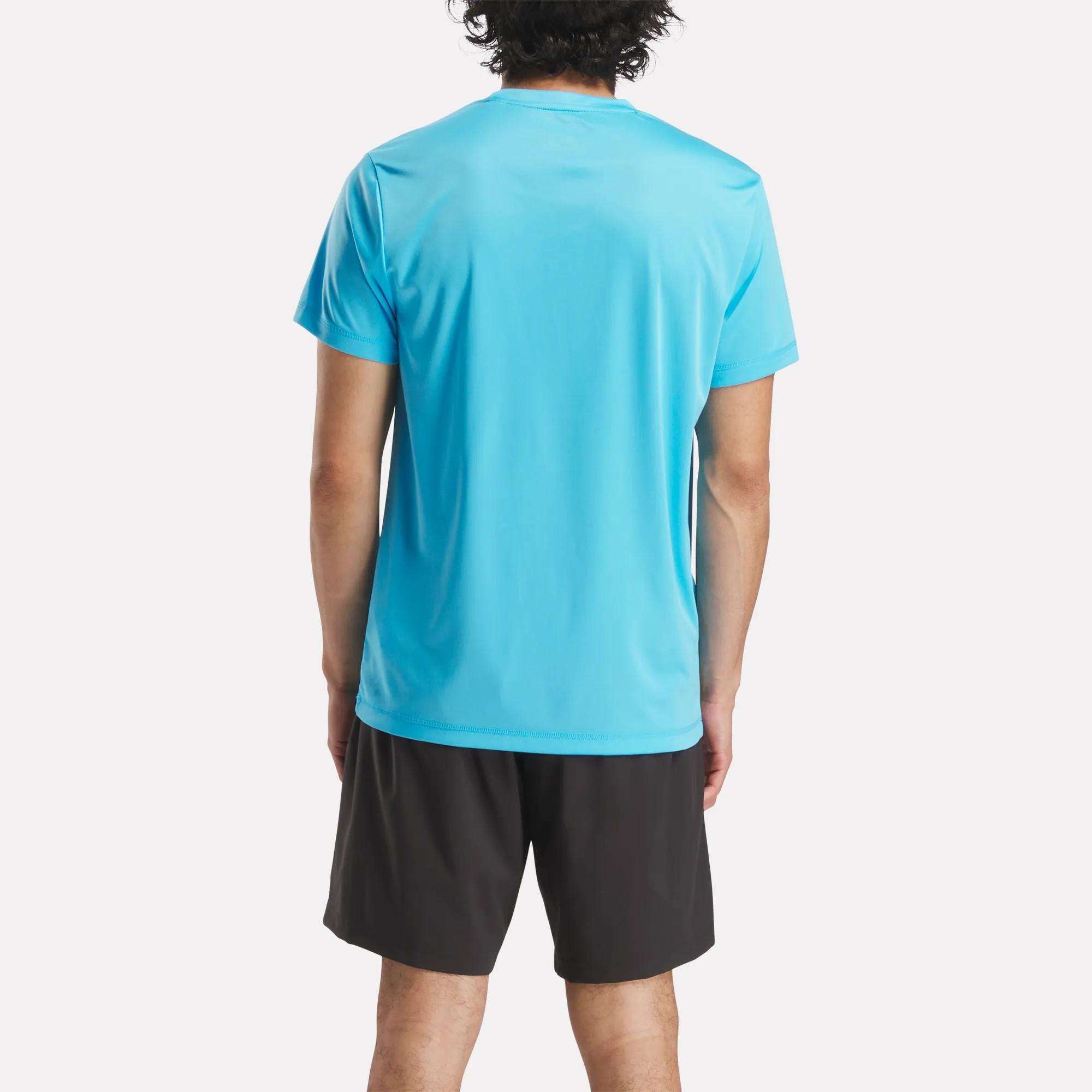A person with short dark hair stands facing away, wearing a bright blue Reebok Men's ID Train Short Sleeve Tech Tee and black shorts against a plain white background.