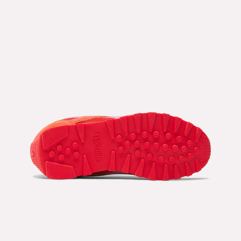 The image displays the bottom view of the Reebok Classic AZ Shoes - Big Kids, featuring a red textured rubber sole with circular and rectangular treads for grip. The Reebok logo appears at the center, appealing to fans of retro sneakers.